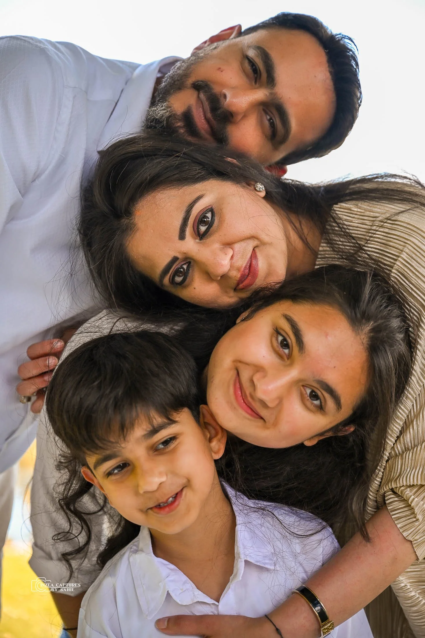A family of four smiling, lying close together, with their heads touching, looking at the camera.