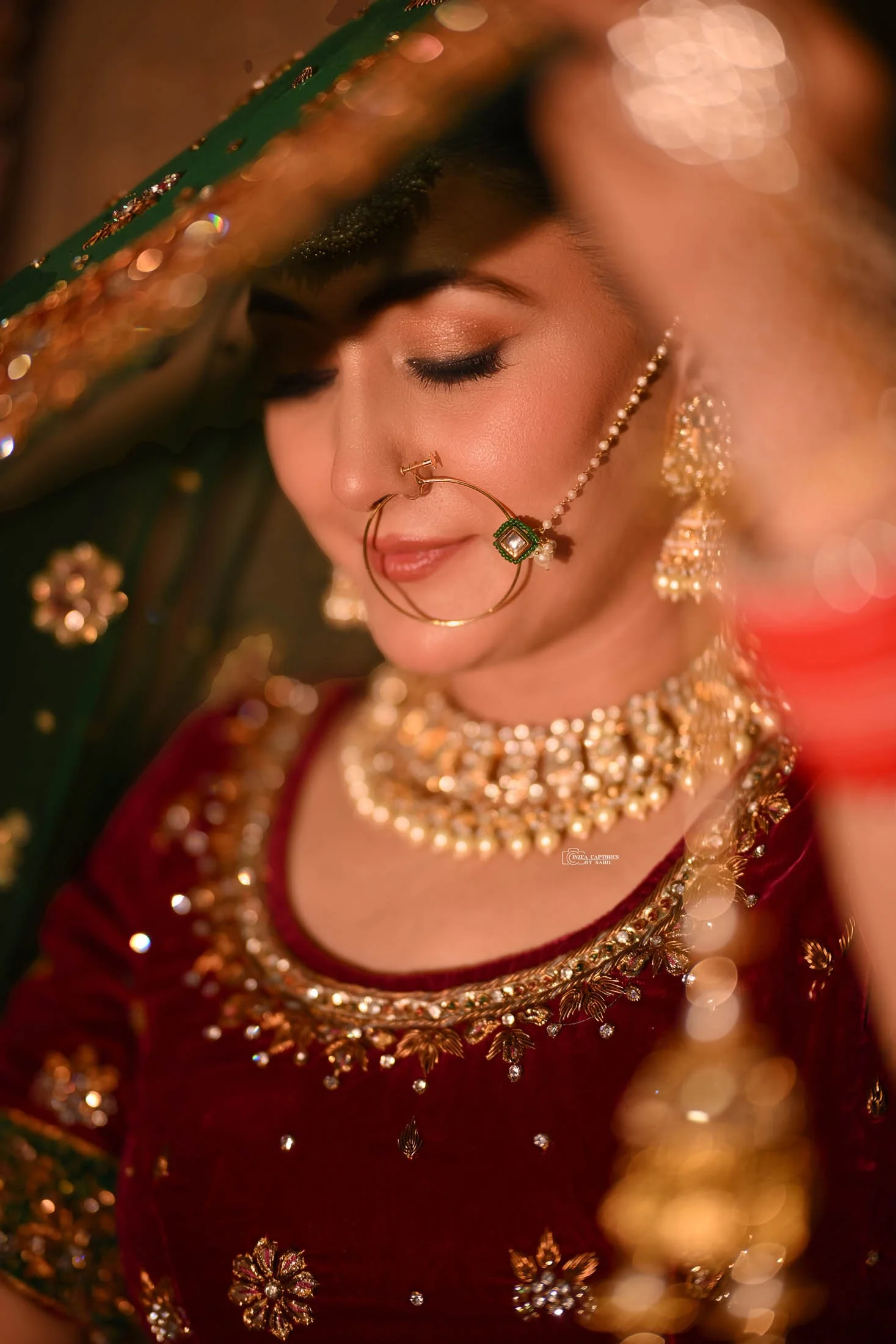 Close-up of a woman dressed in traditional Indian attire, wearing intricate jewelry, including a necklace, earrings, and a nose ring, with her eyes closed and a serene expression.