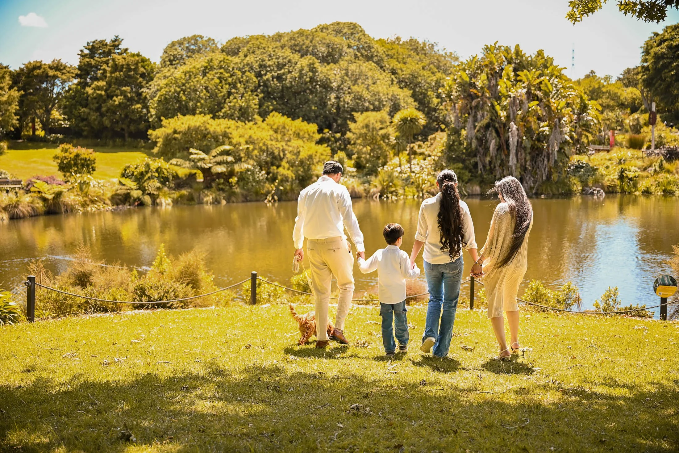 Family walking by a pond in a park on a sunny day.