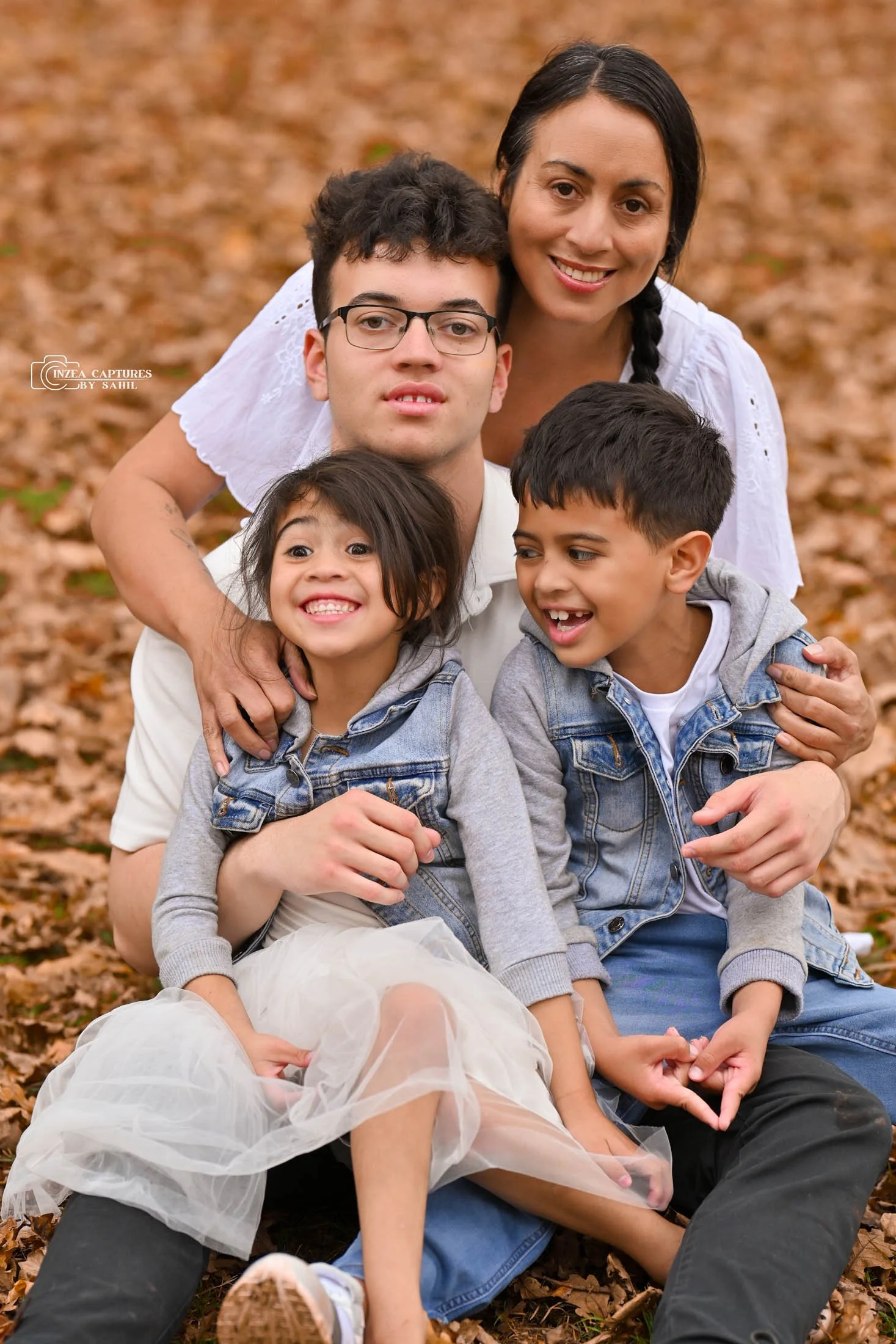 Family of five sitting on autumn leaves, smiling and hugging outdoors.