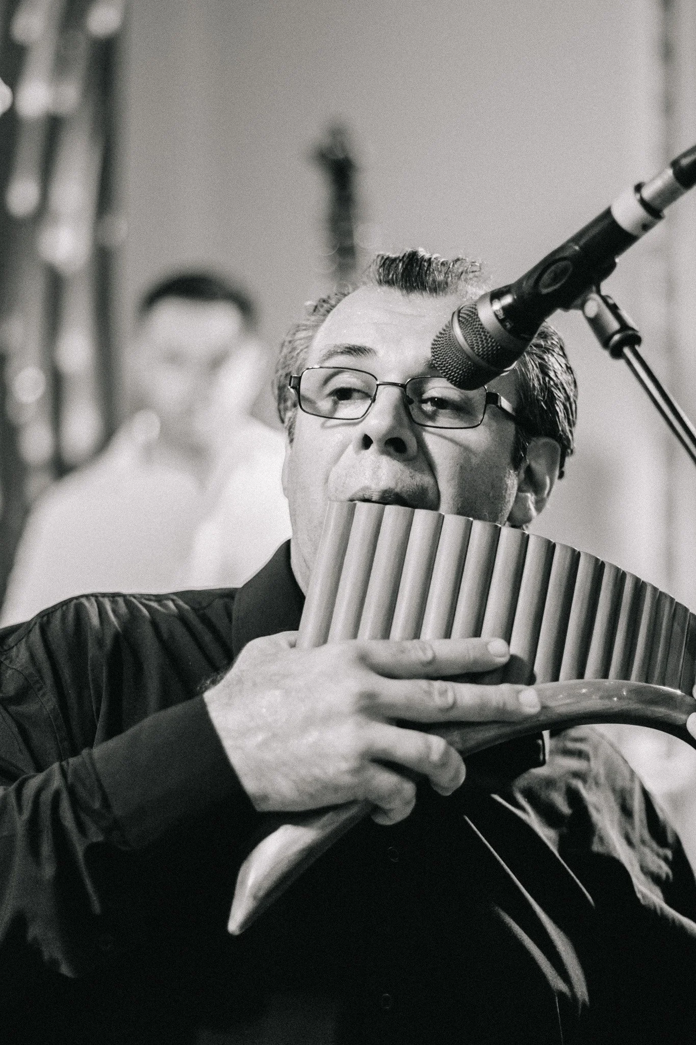 A man in glasses playing a pan flute near a microphone.