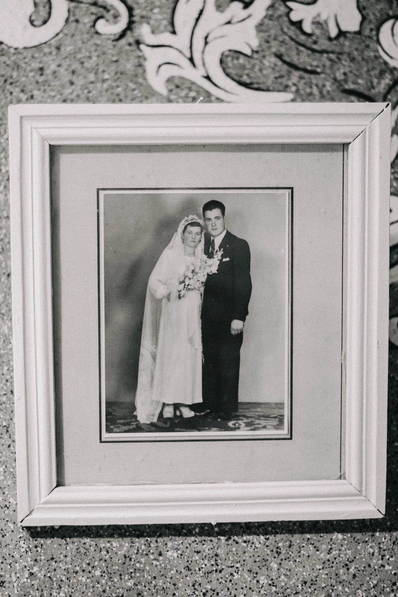 A black and white portrait of a bride and groom in wedding attire inside a white frame, on a speckled surface.