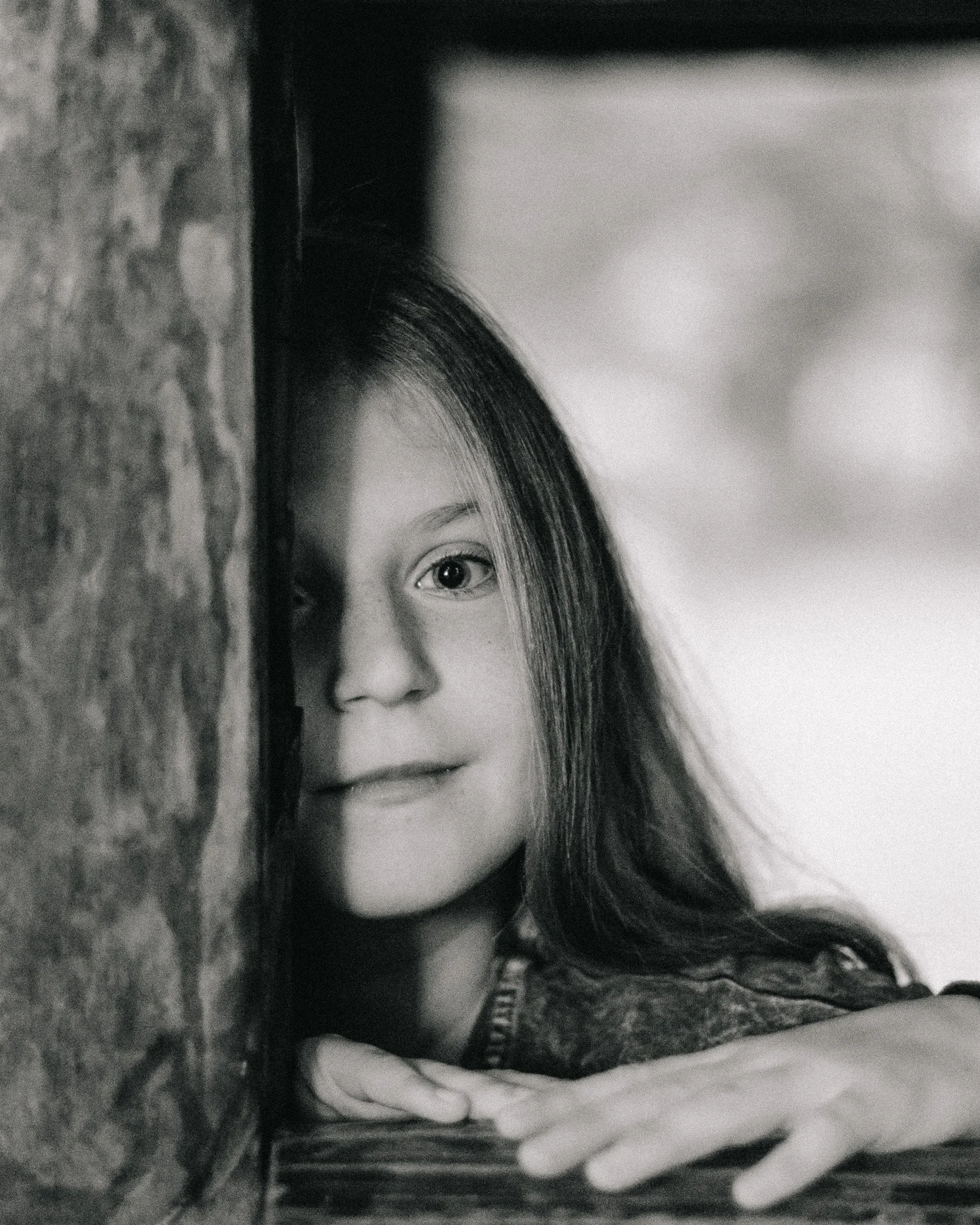 A young girl with long hair peering around a corner in black and white.