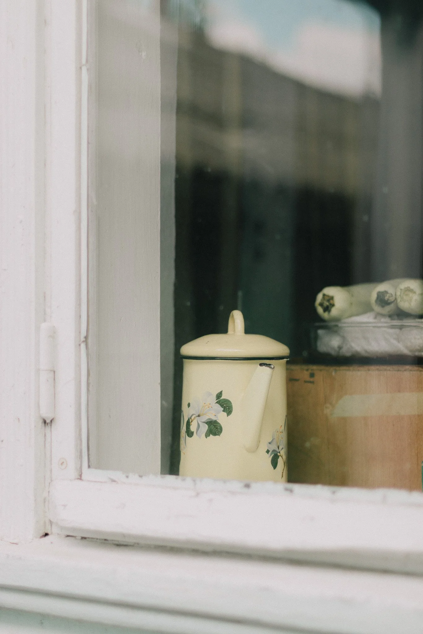 A cream-colored teapot with floral design seen through a window.