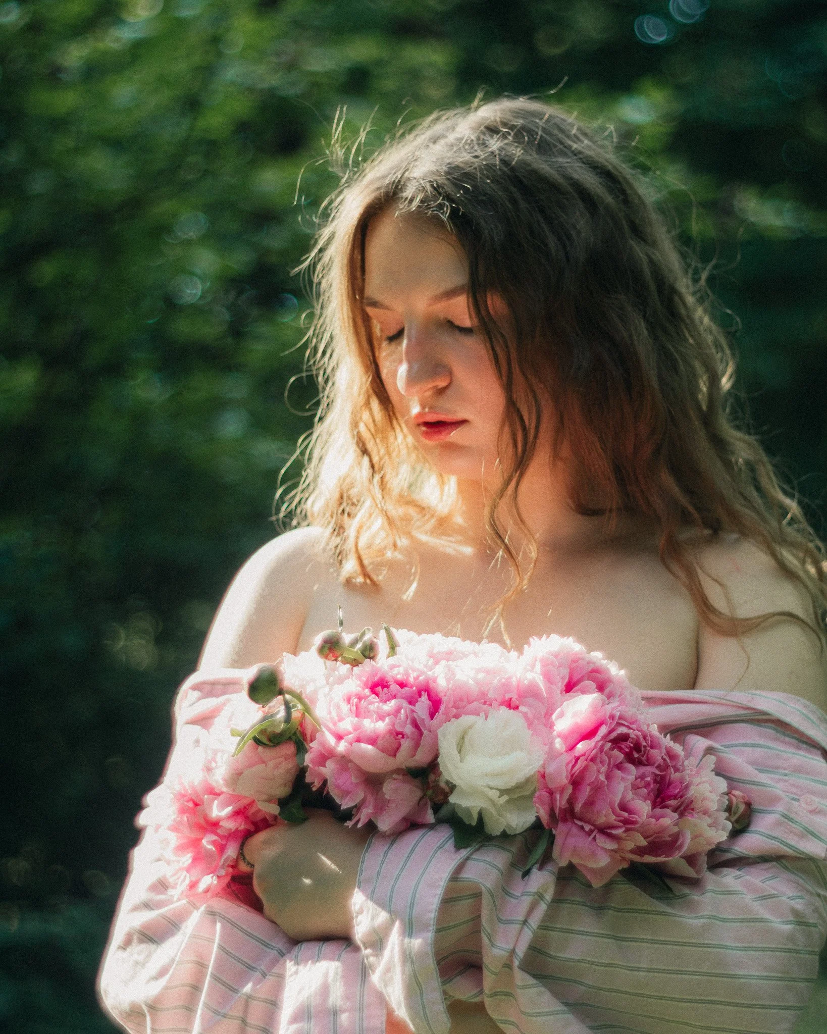 Young woman with long, wavy hair holding a bouquet of pink and white peonies outdoors in natural sunlight.