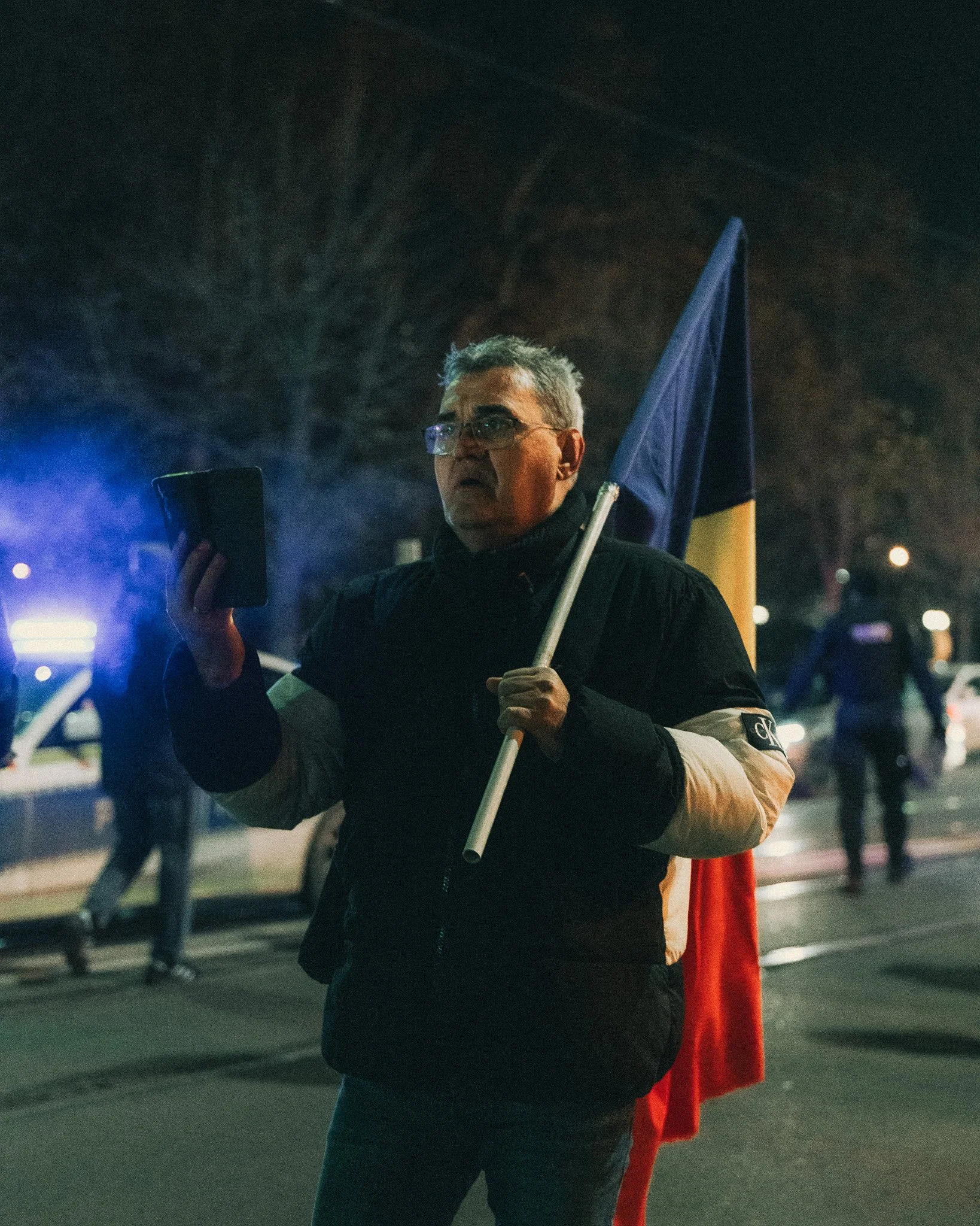 A man holding a flag and a phone at night during a protest or demonstration.