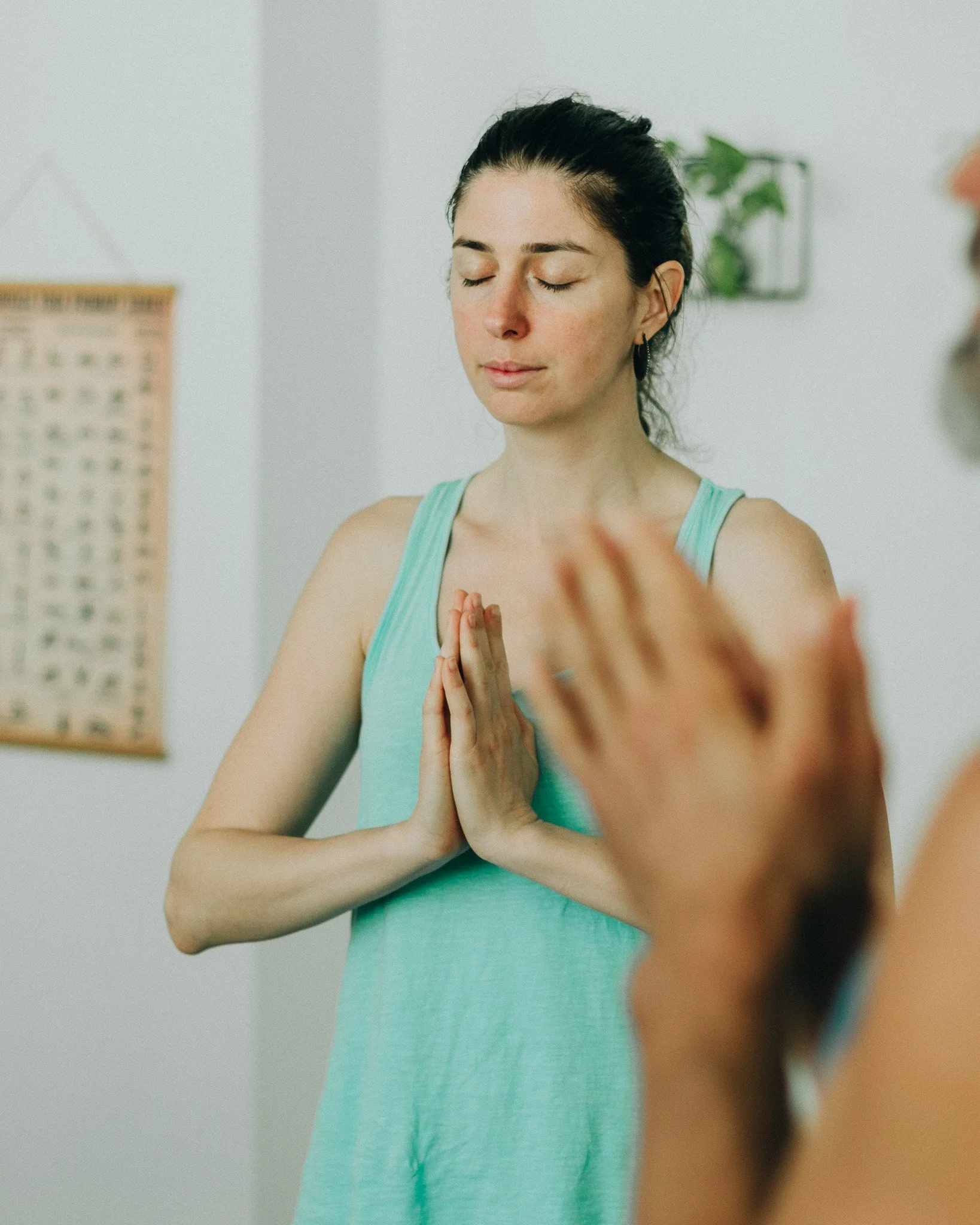 A woman in a yoga pose with hands in prayer position, eyes closed, and a calm expression.
