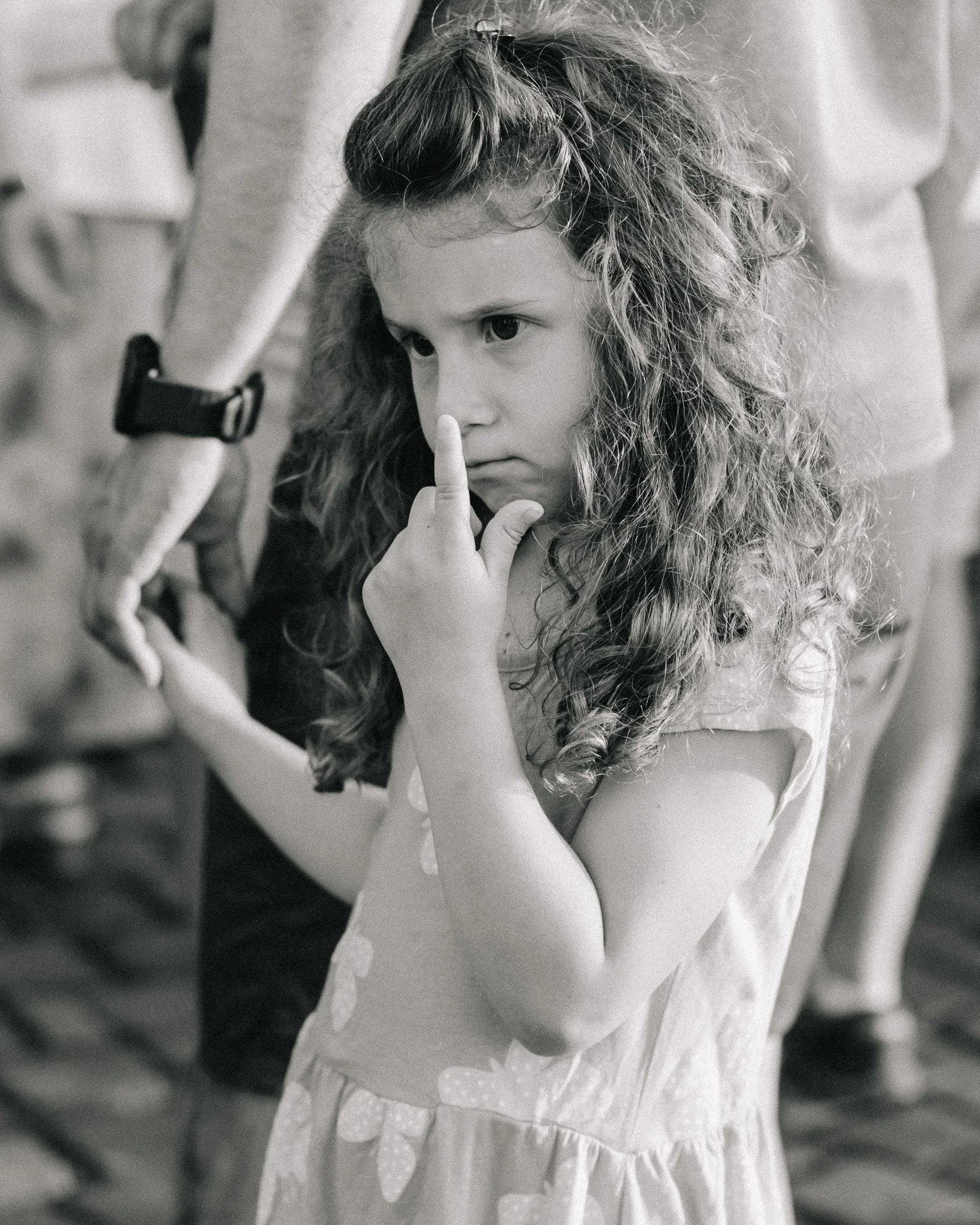 A young girl with curly hair making a gesture to her lips with her index finger in front of her face.