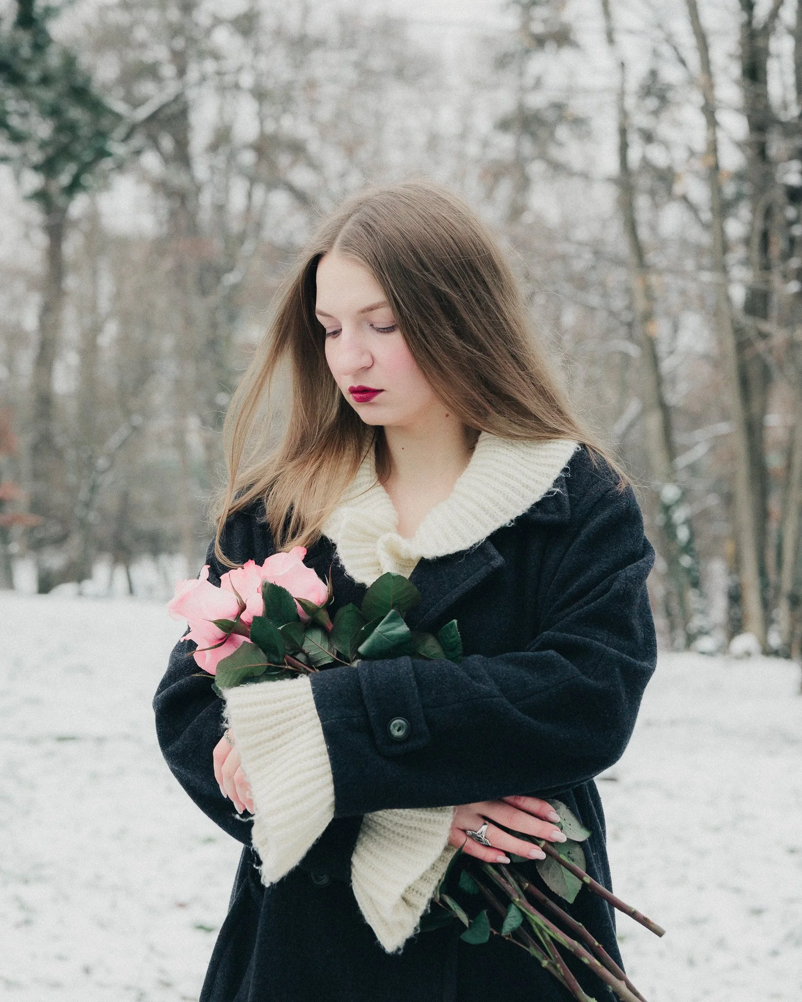 A young woman with long hair holding a bouquet of pink roses in a snowy outdoor park.