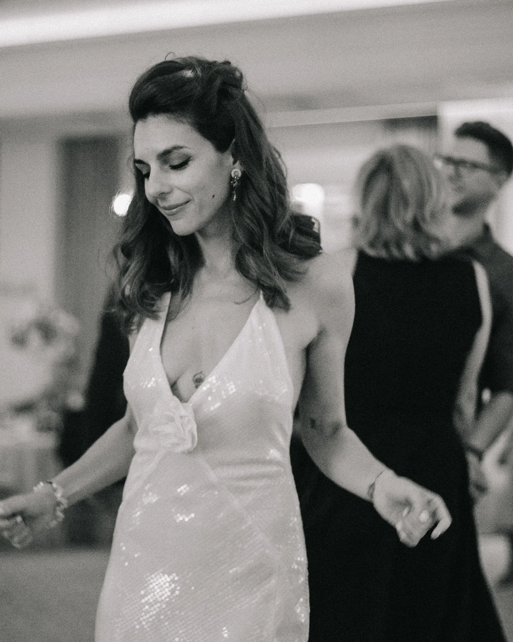 A woman with wavy hair in a fancy dress, smiling with eyes closed at a social event.