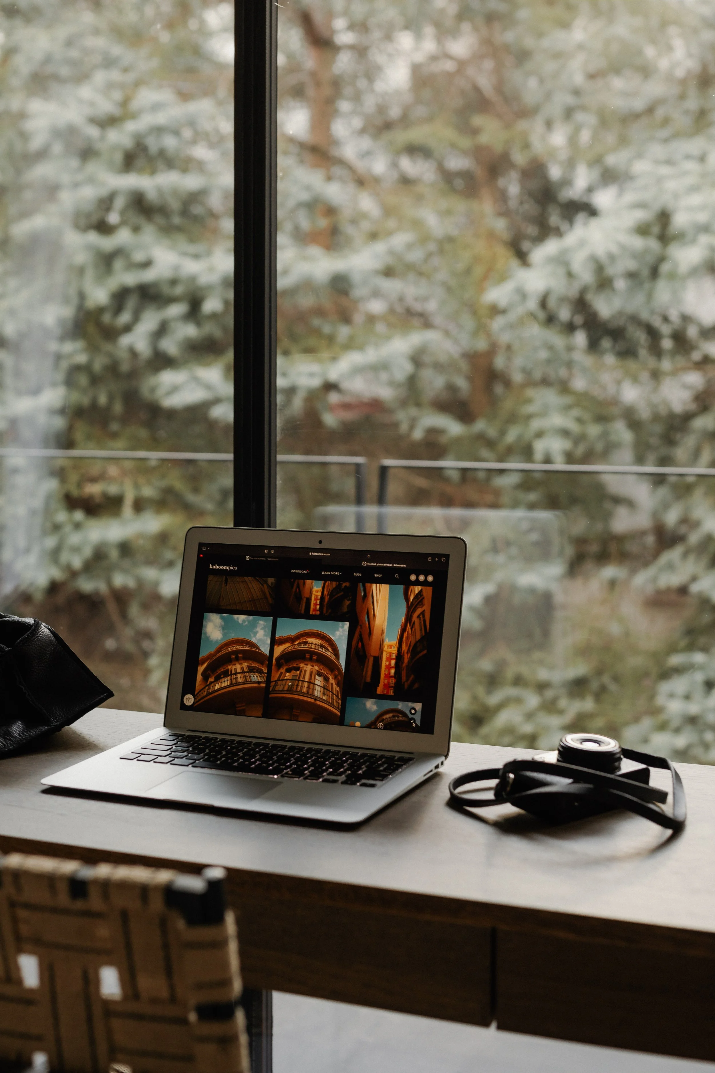 A laptop on a wooden table displaying a photo gallery of building architecture with a window showing snow-covered trees outside.
