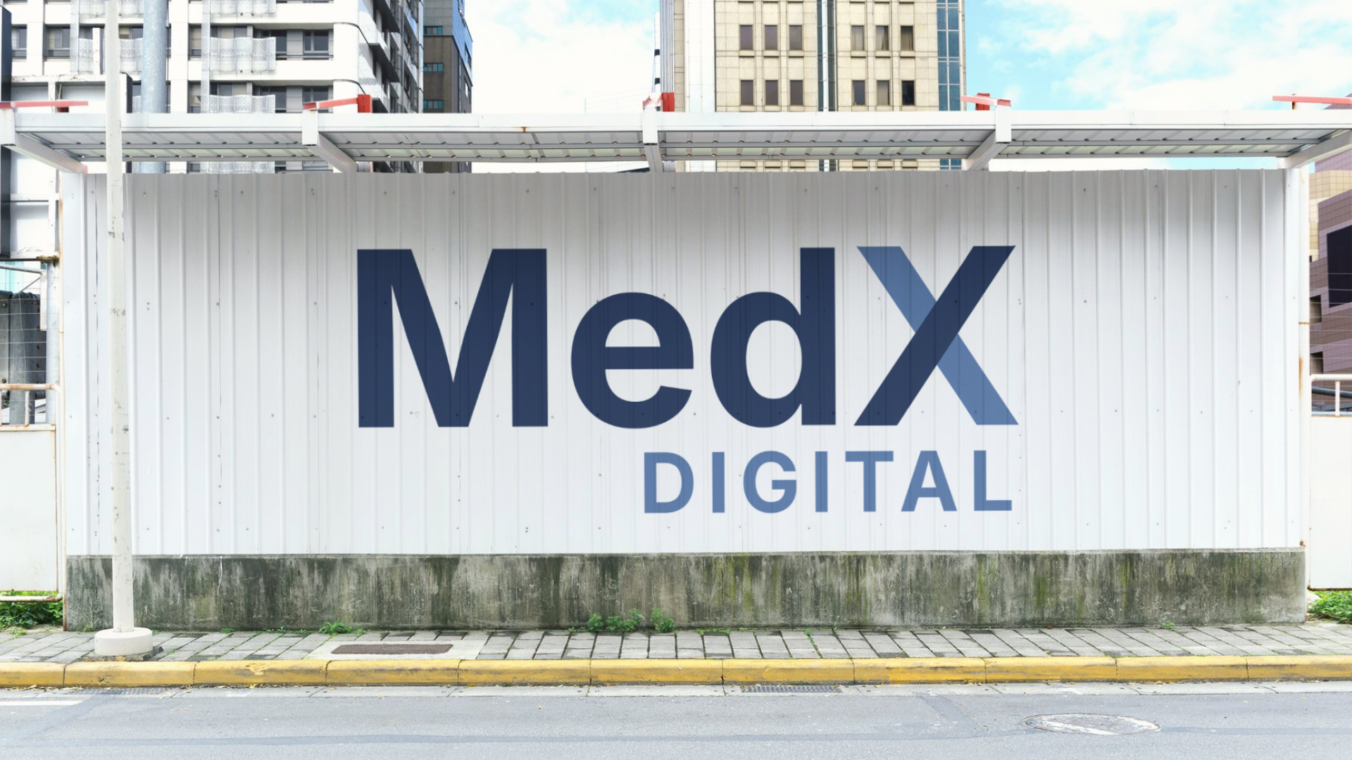 Large white wall with the word 'MedX' in bold black letters and 'DIGITAL' in smaller blue letters underneath, located in an urban area with tall buildings in the background.