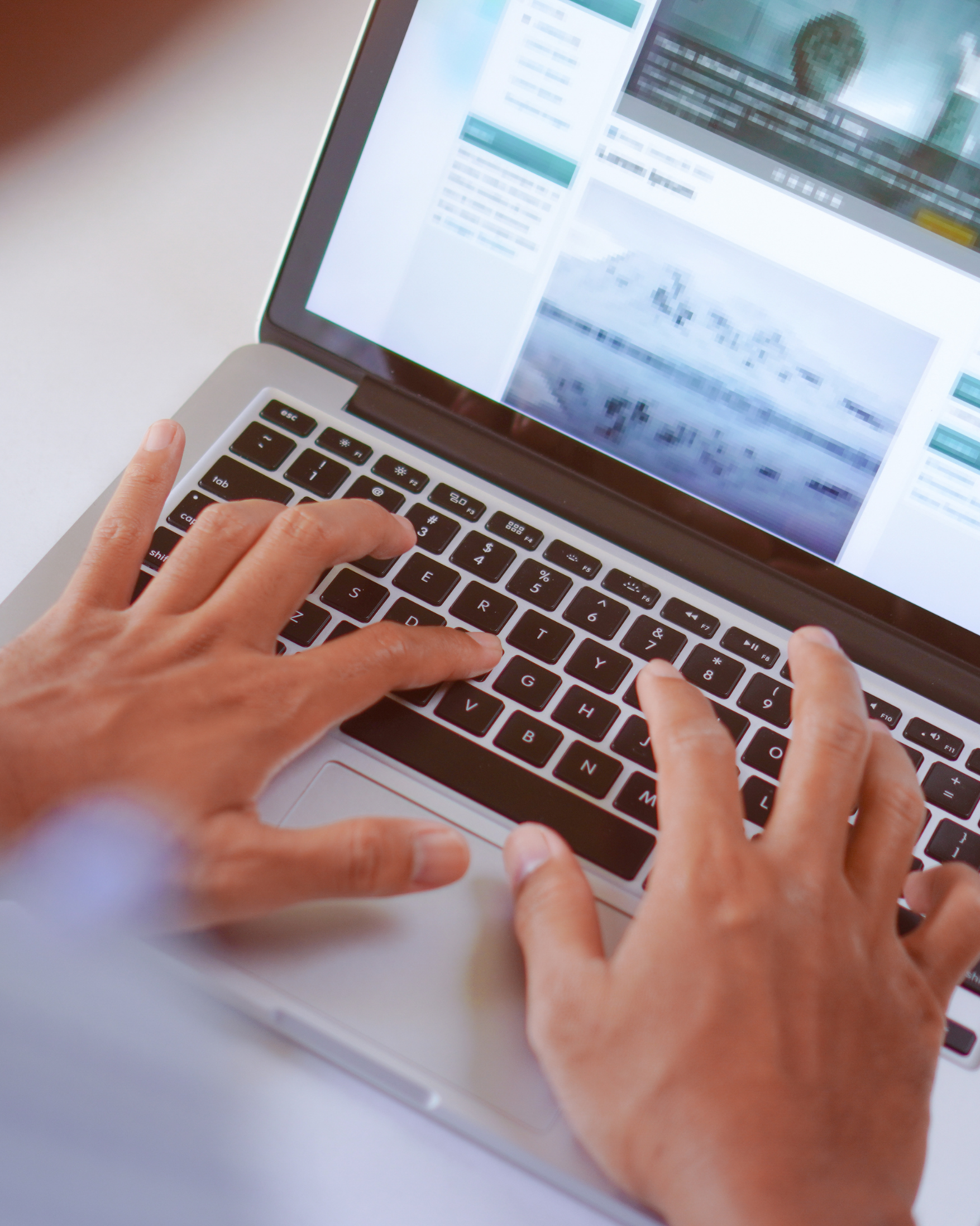 Close-up of a person's hands typing on a silver laptop keyboard with a website or document displayed on the screen.