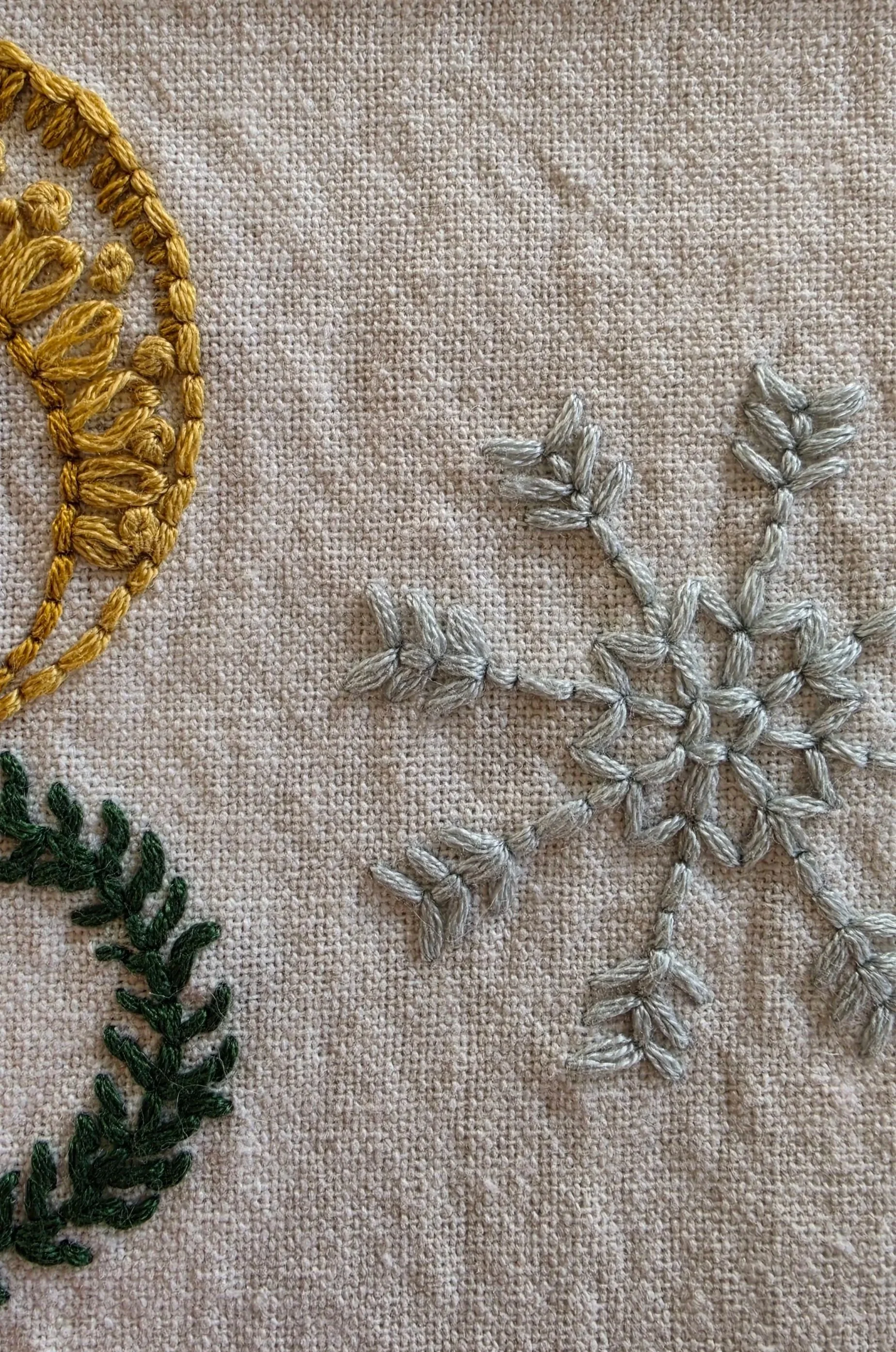 Close-up of delicate blue-green embroidery stitches on natural cotton fabric beside the angel design.