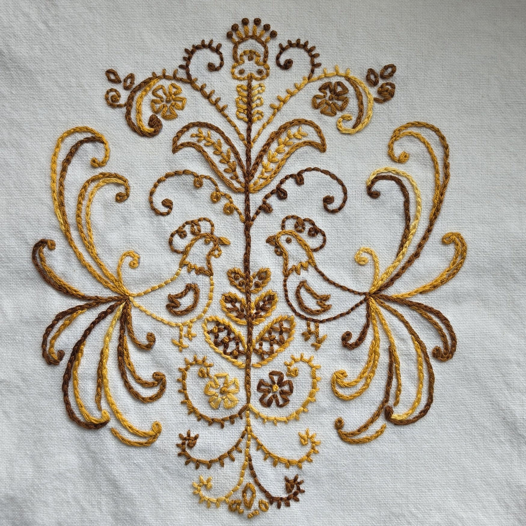 Close-up of hand embroidered farmhouse chickens, flowers and scrollwork on cream cotton-colored cotton kitchen towel