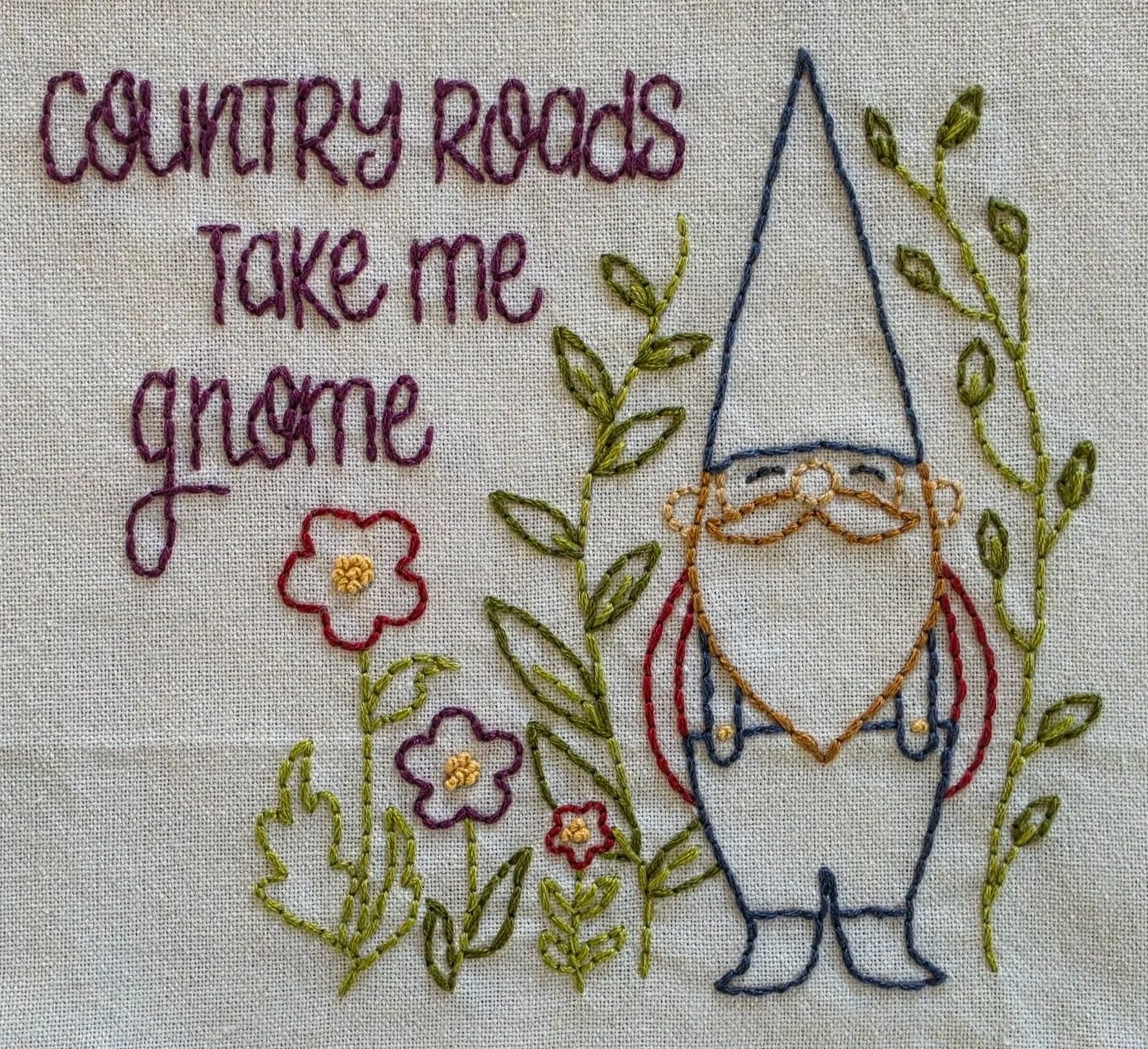 Full view of the hand-embroidered gnome, wildflowers, greenery, and Country Roads Take Me Gnome lettering.