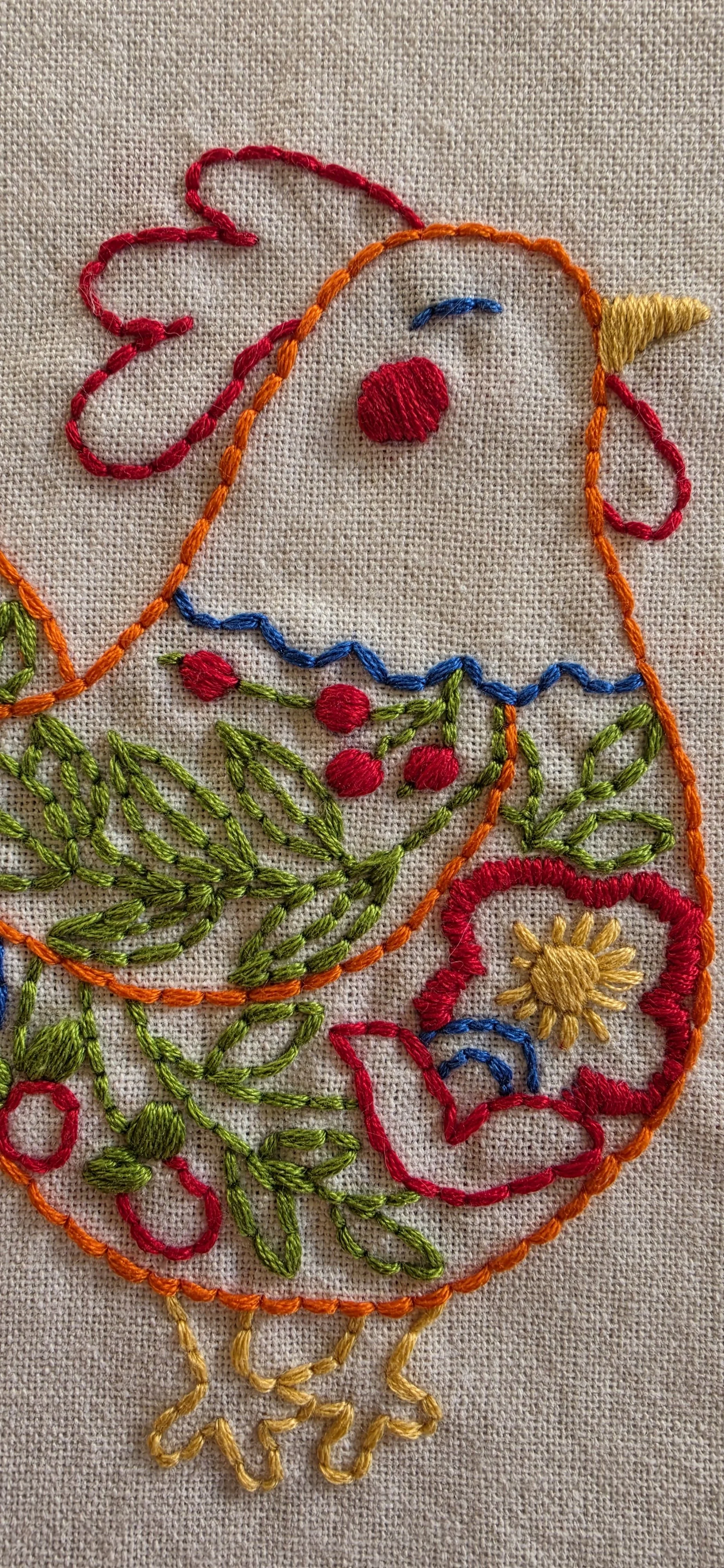 Close-up of colorful flowers, green leaves, and decorative stitching on the embroidered hen.