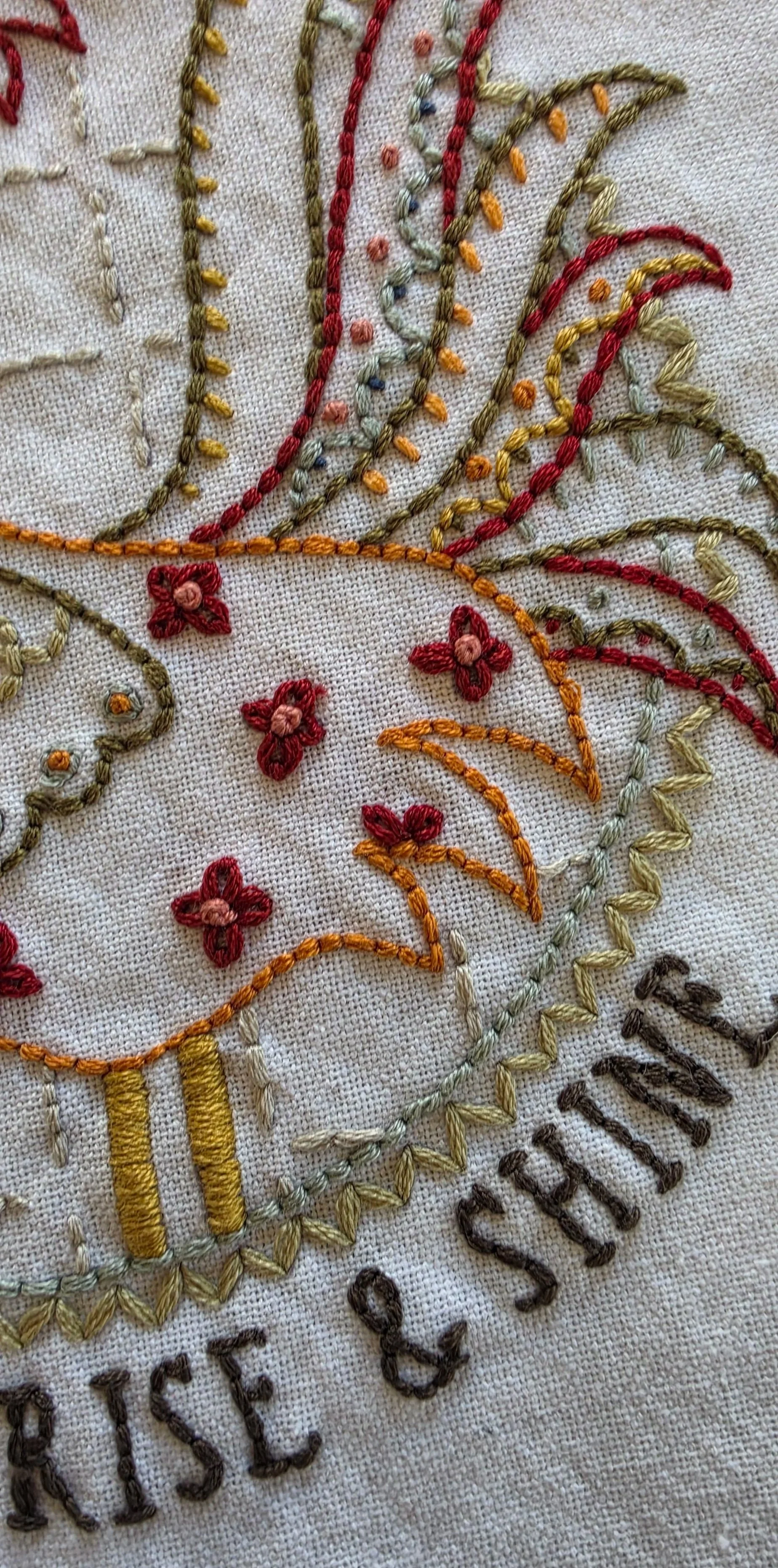 Hand-embroidered Rise & Shine rooster design with colorful folk-art stitching on a cream kitchen towel.