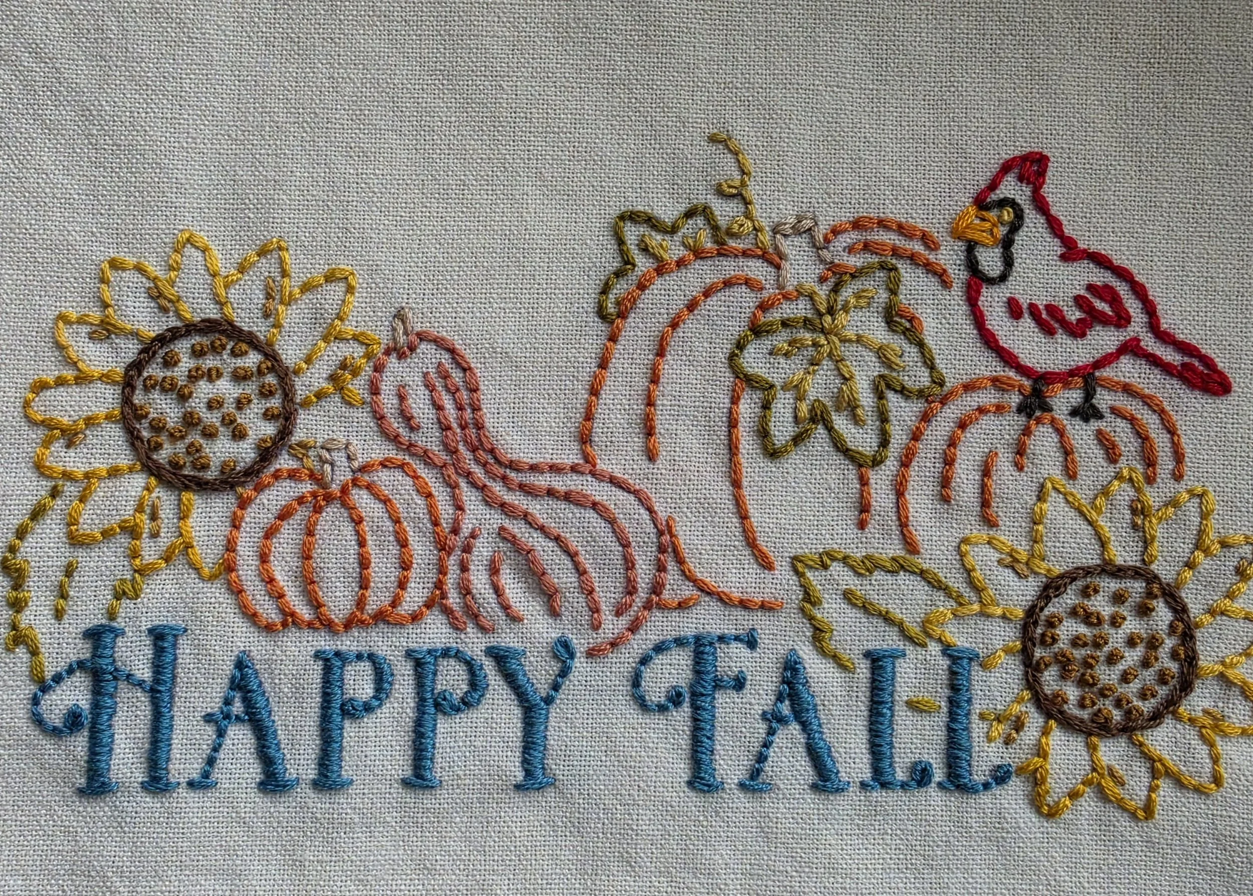 Close-up of hand embroidered Happy Fall design with pumpkins, sunflowers, leaves and cardinal on cream cotton kitchen towel.