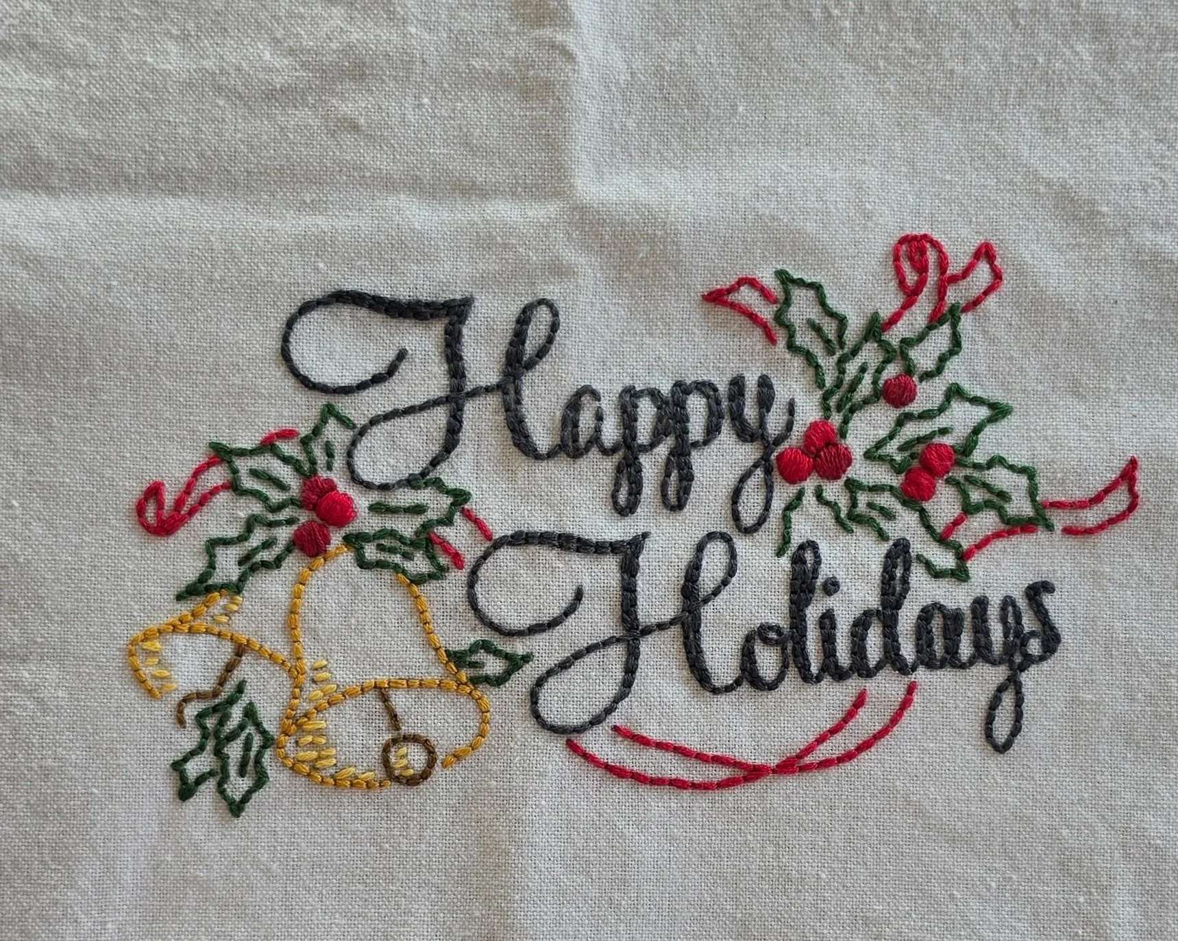 Full view of Happy Holidays lettering surrounded by embroidered holly leaves, red berries, and greenery.