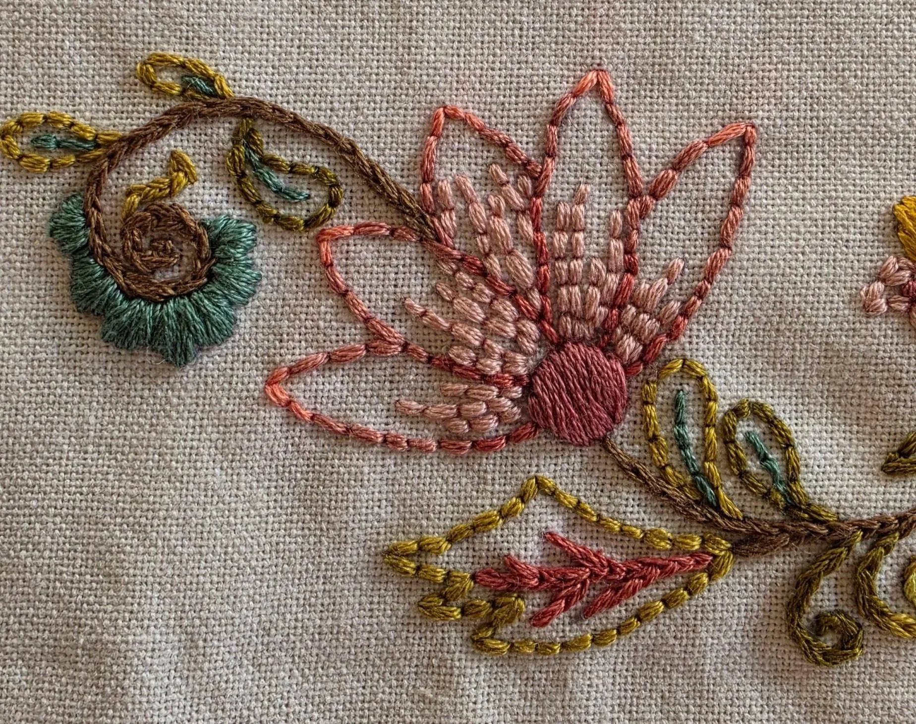 Close-up of pink hand-embroidered flower petals and green leaves on the floral vine kitchen towel.
