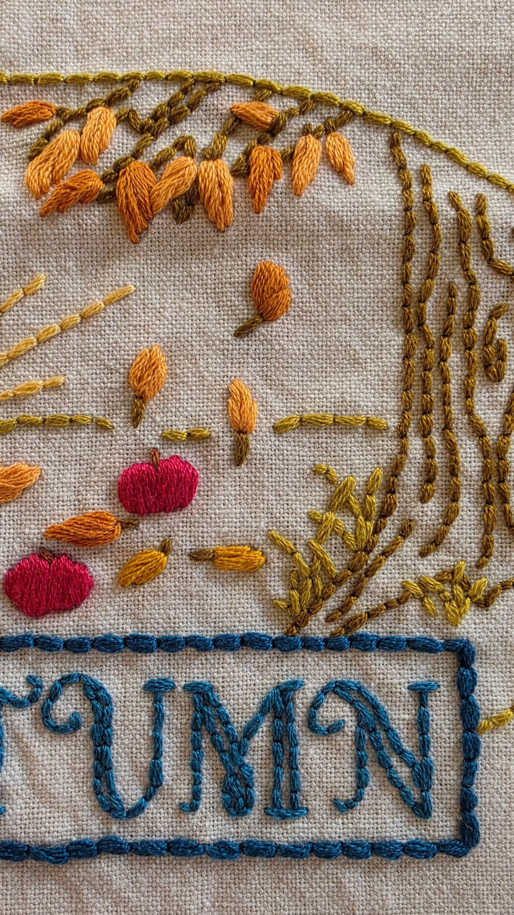 Close-up of orange falling leaves, red apples, and a tree stitched on a natural beige autumn towel.