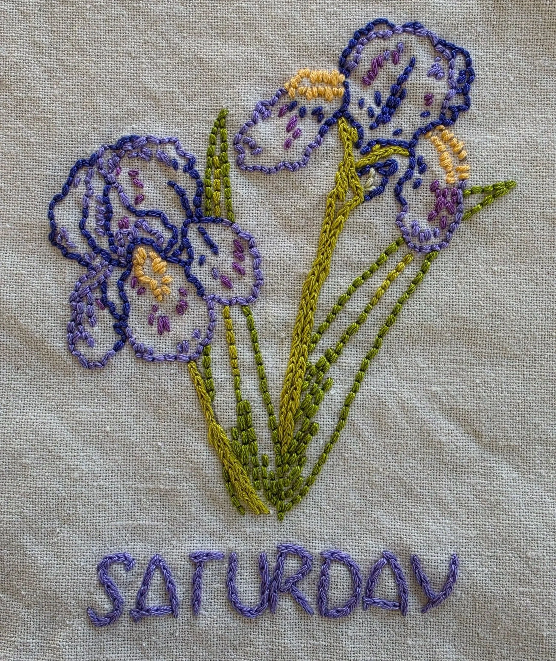 Close-up of purple and lavender iris embroidery with green stems on a cream cotton towel.