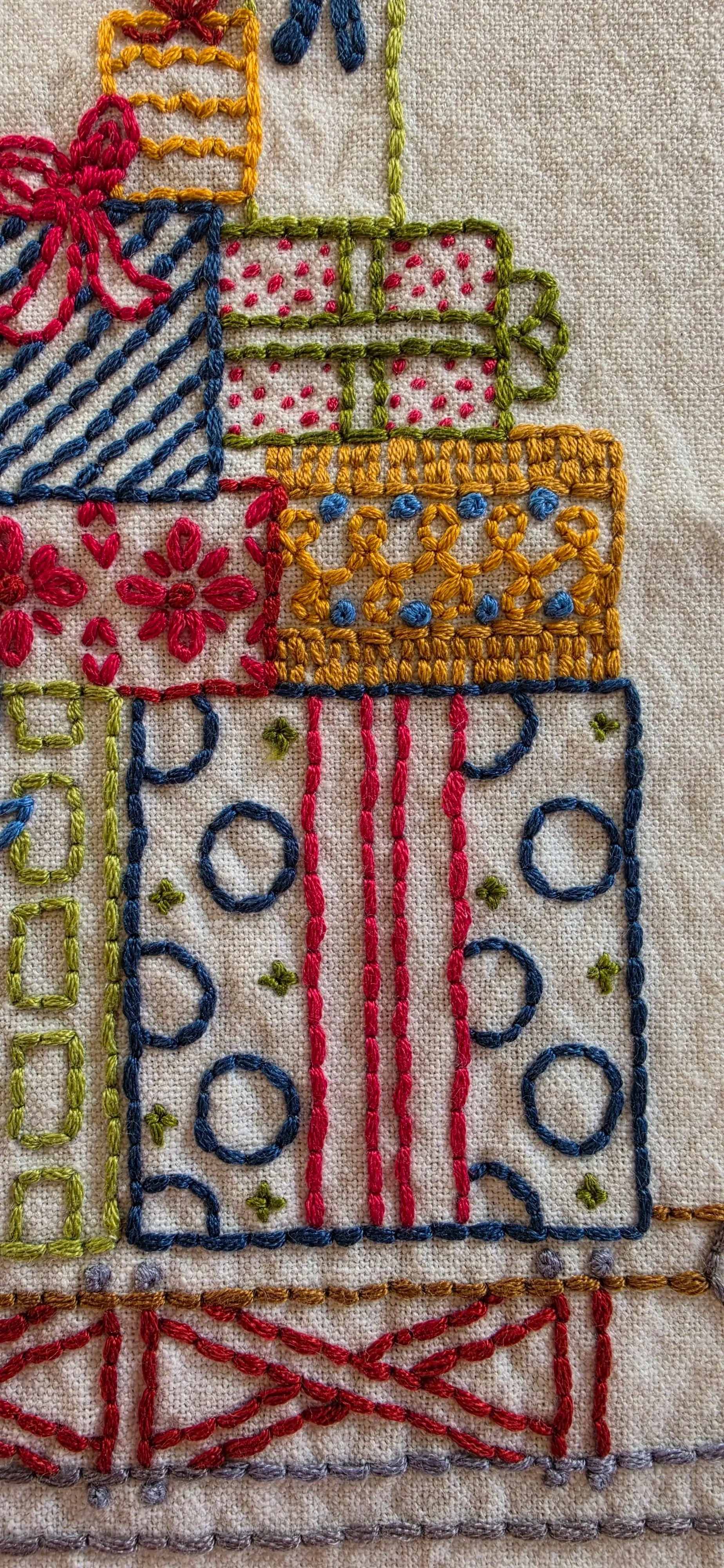 Close-up of detailed hand embroidery on Christmas presents, featuring colorful thread, decorative patterns, and red ribbon accents.
