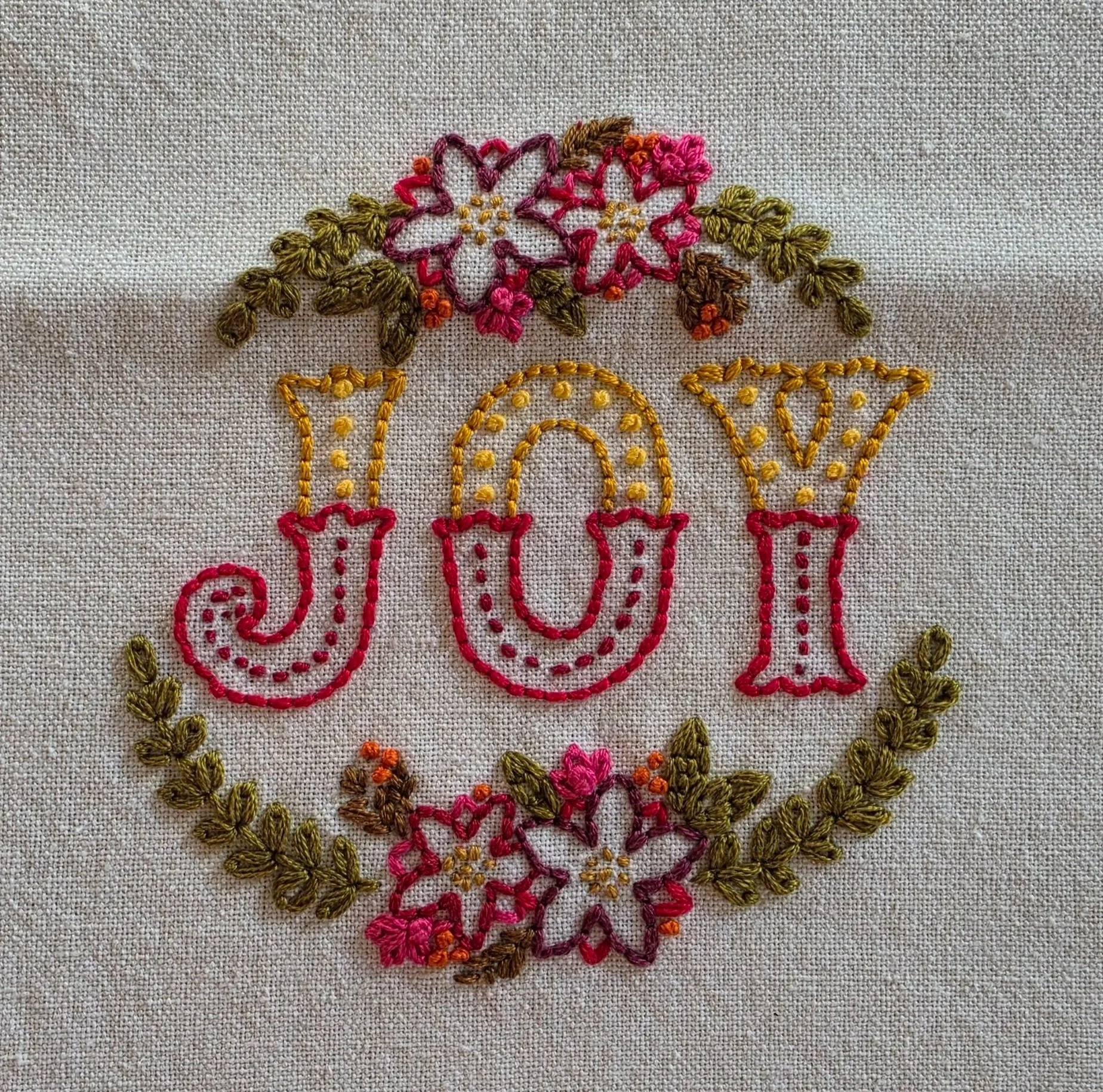 Full floral wreath design surrounding JOY embroidered on a cotton kitchen towel.