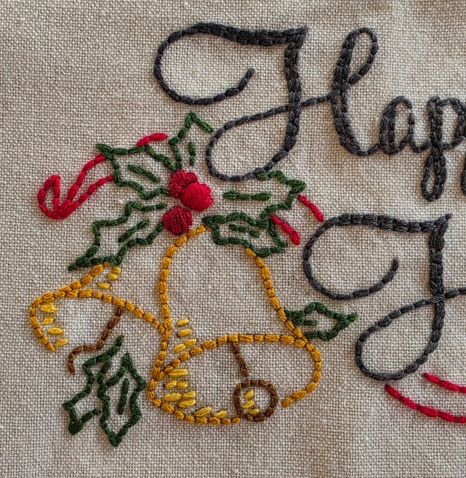 Close-up of hand-embroidered holly leaves, red berries, and decorative greenery on a holiday kitchen towel.