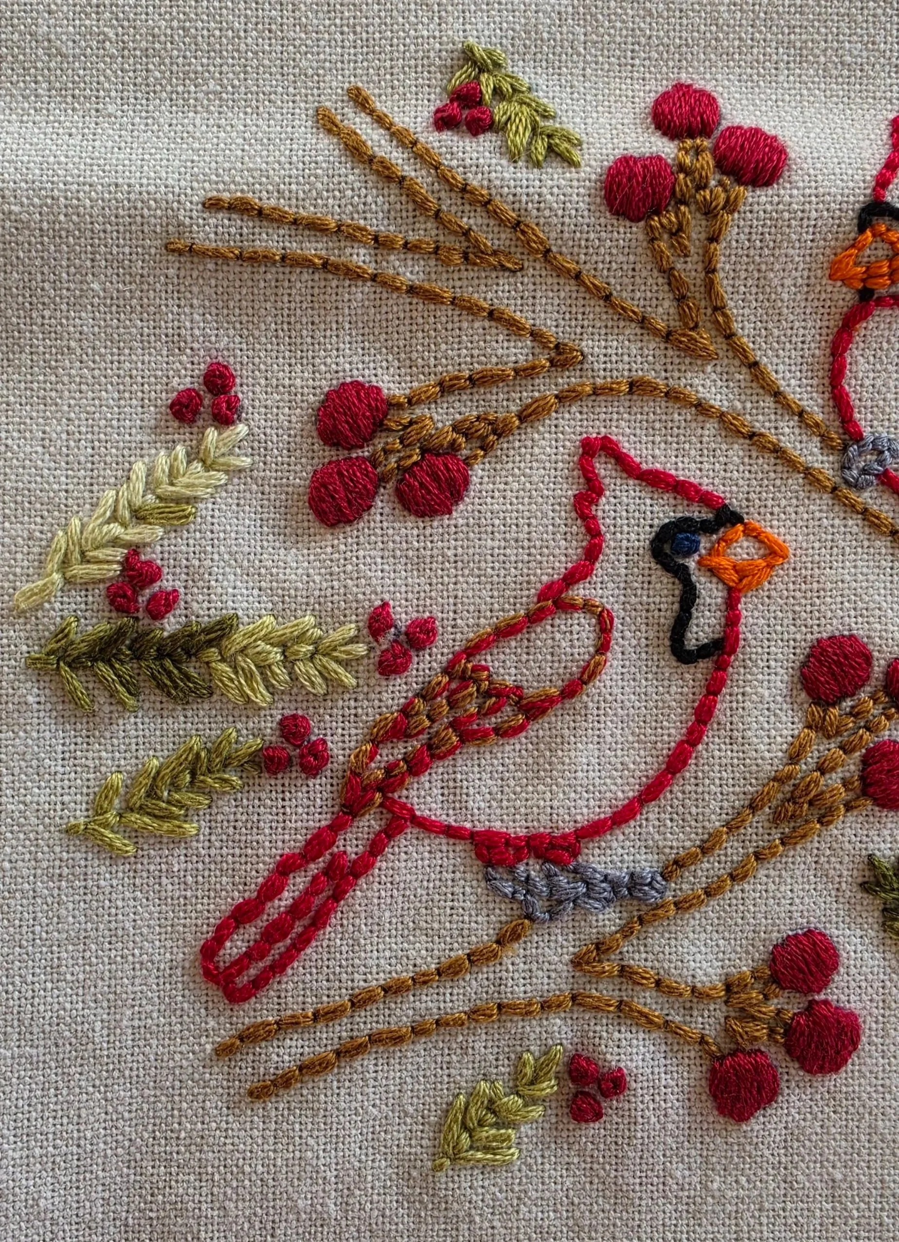 Close-up of hand-stitched cardinals and berry branches showing the colorful embroidery on textured fabric.
