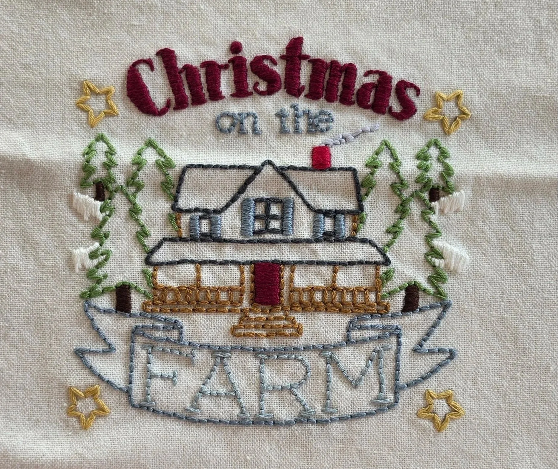 Full view of the hand-embroidered Christmas on the Farm design featuring a farmhouse and evergreen trees.