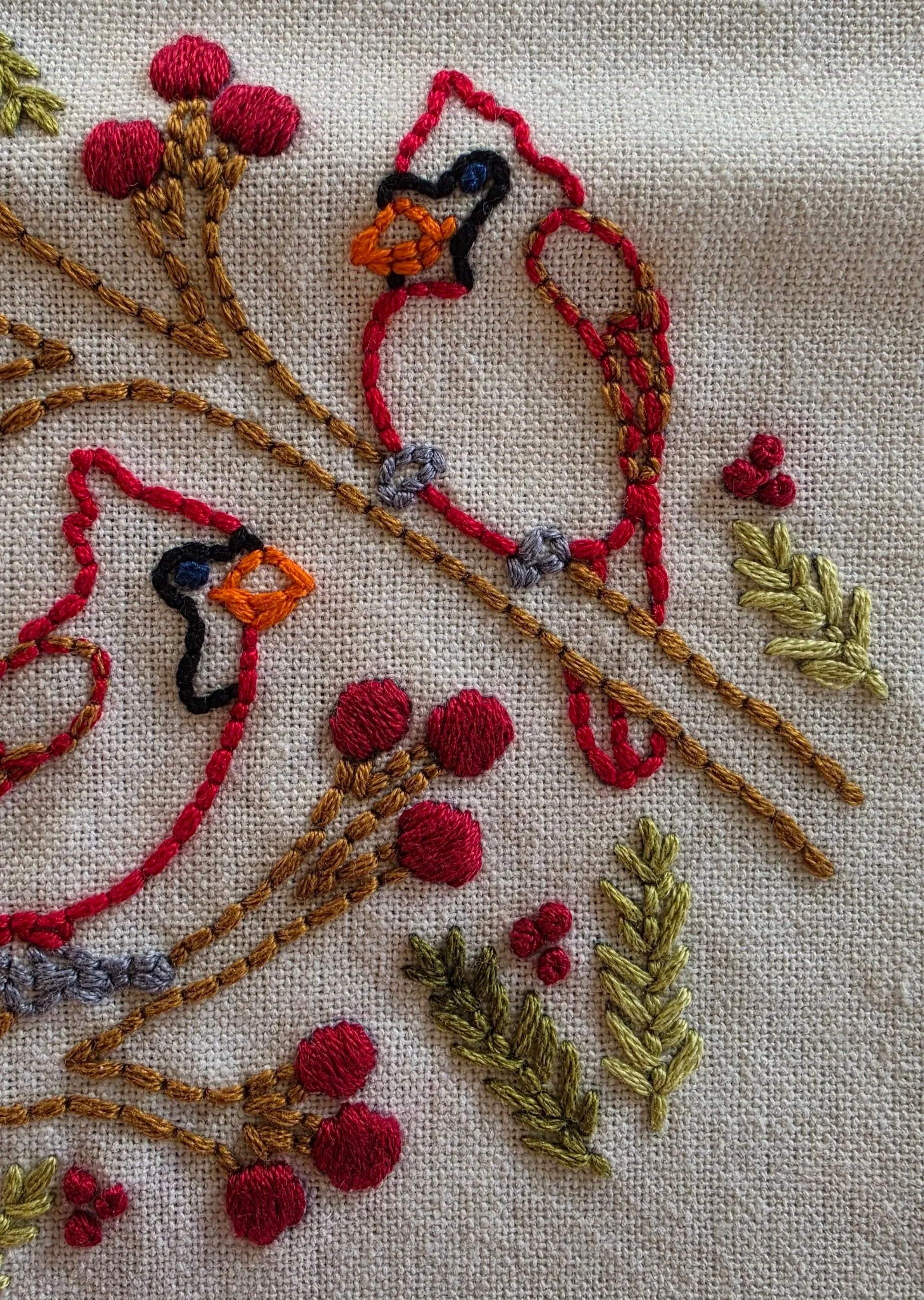 Detailed view of a hand-embroidered cardinal among berry clusters and leafy branches.
