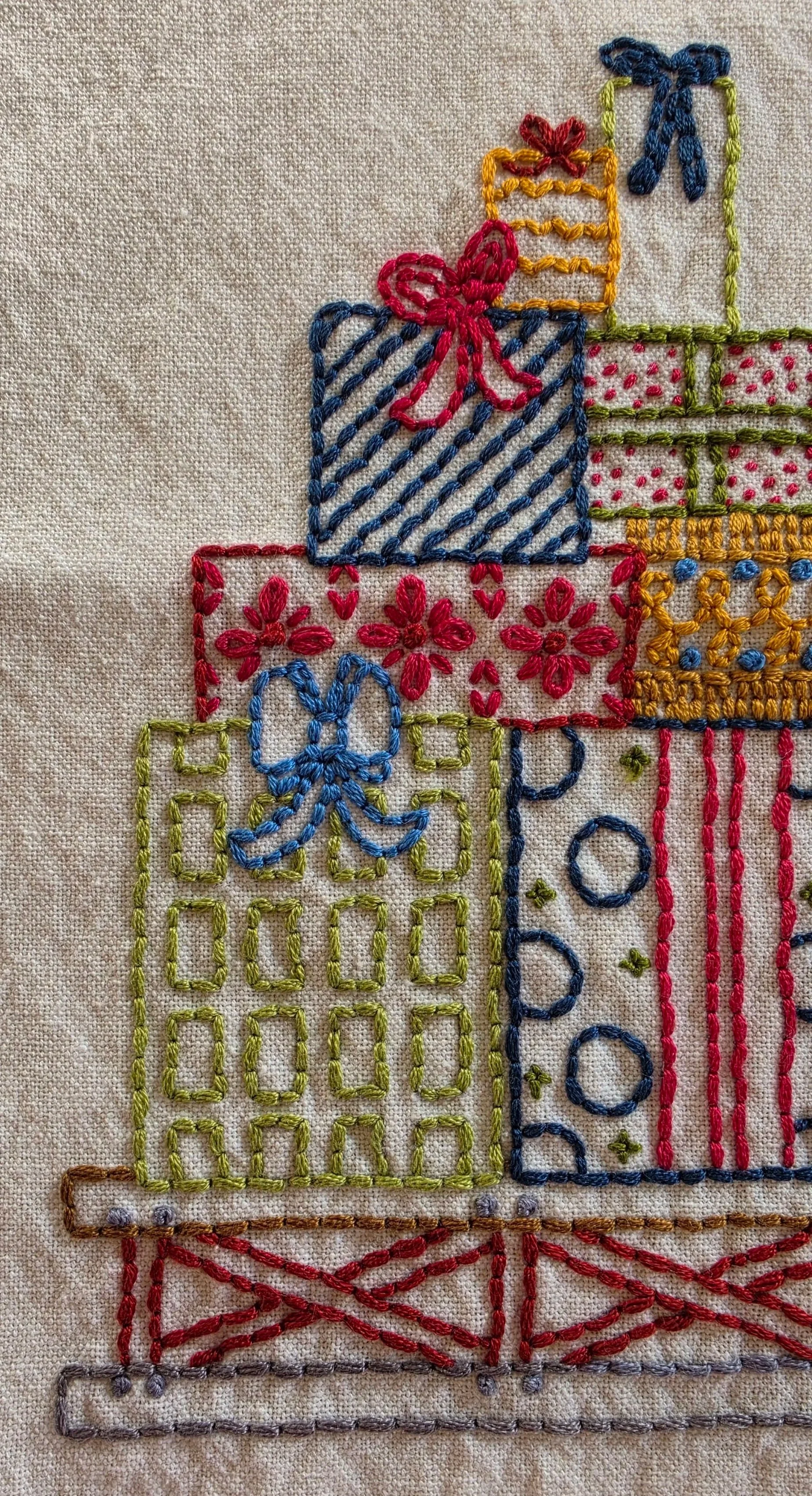 Close-up of colorful hand-embroidered Christmas presents with patterned wrapping, stripes, polka dots, and bows.