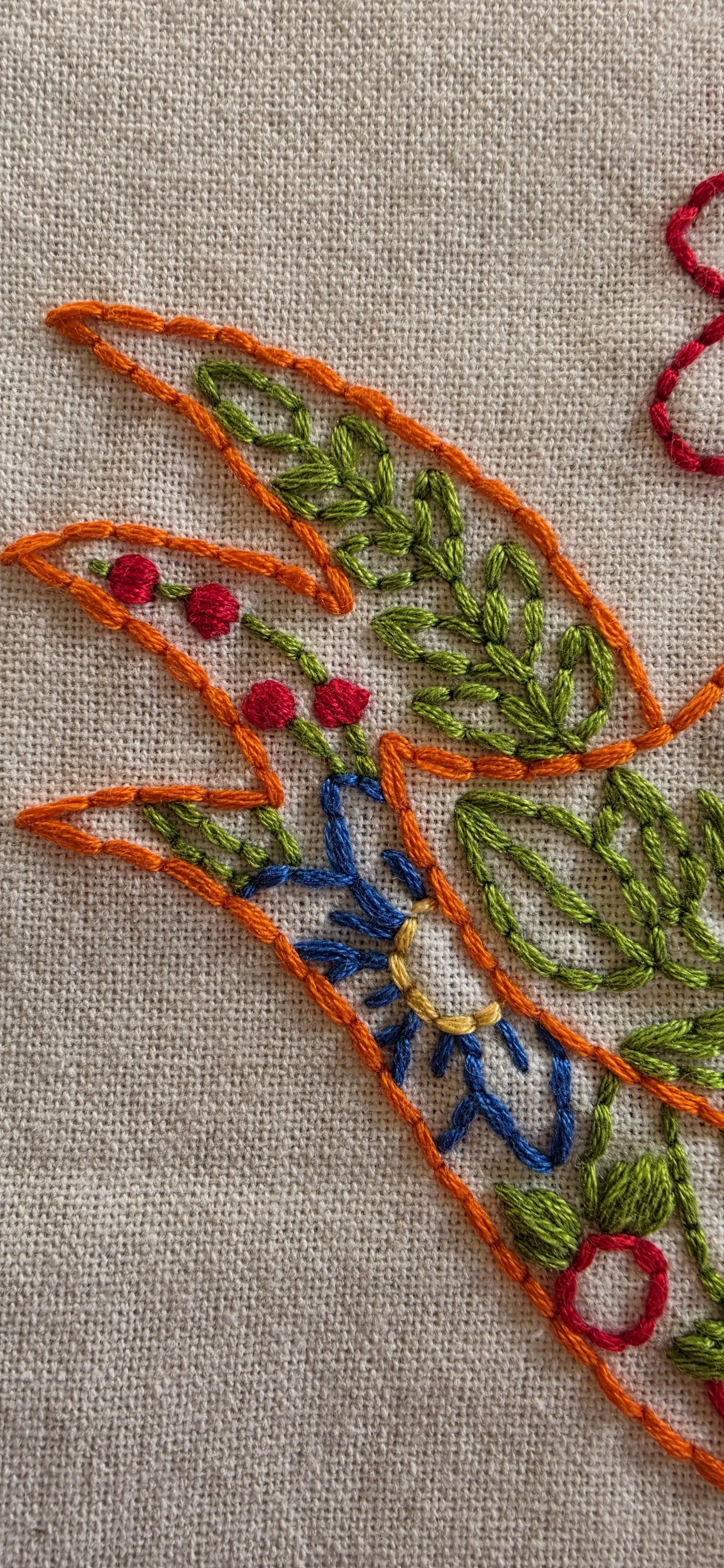 Detailed hand embroidery showing the hen's colorful feathers, red and blue accents, and decorative floral stitching.