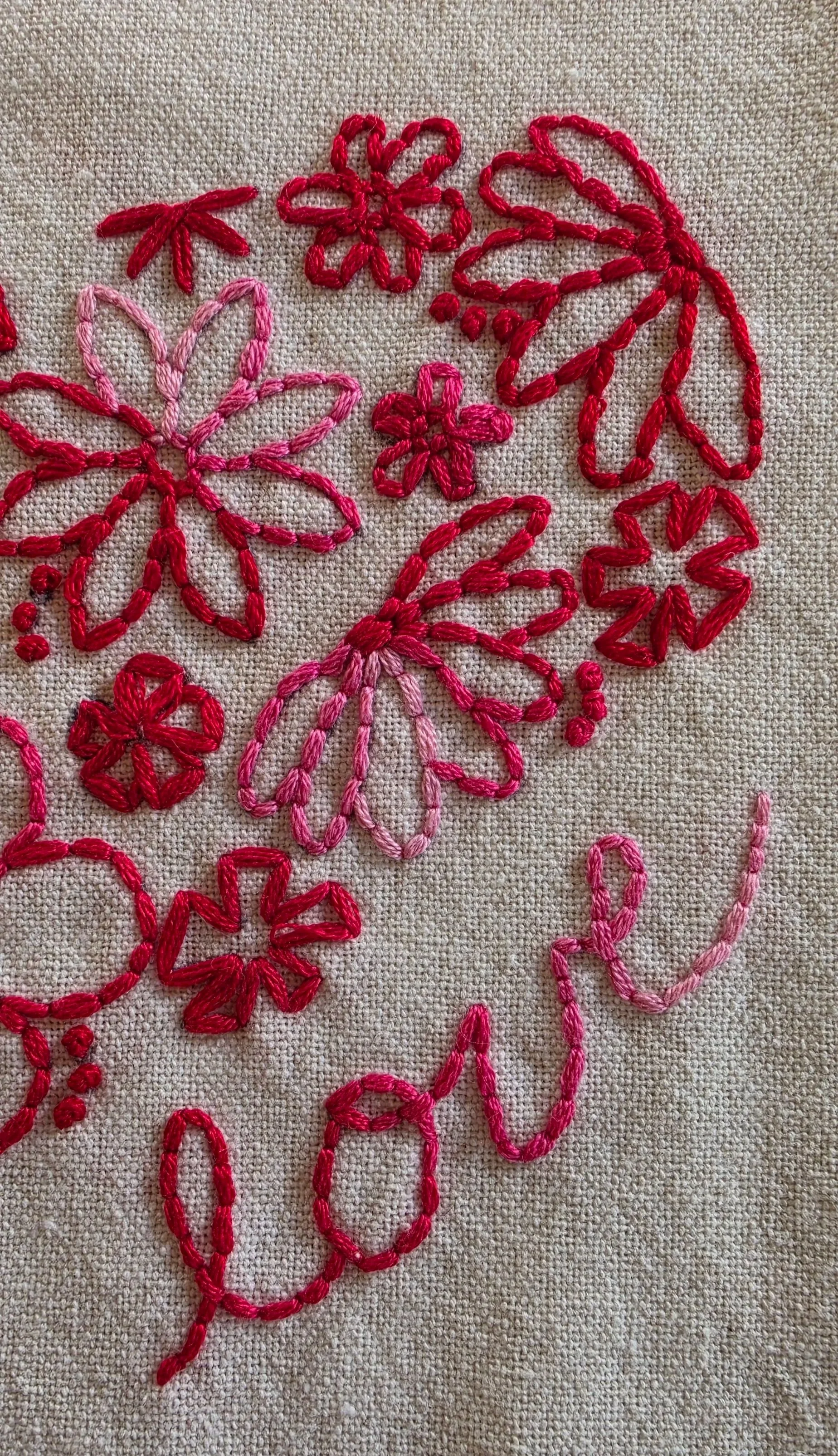 Close-up of red and pink hand-embroidered flowers and decorative stitches on a white kitchen towel.