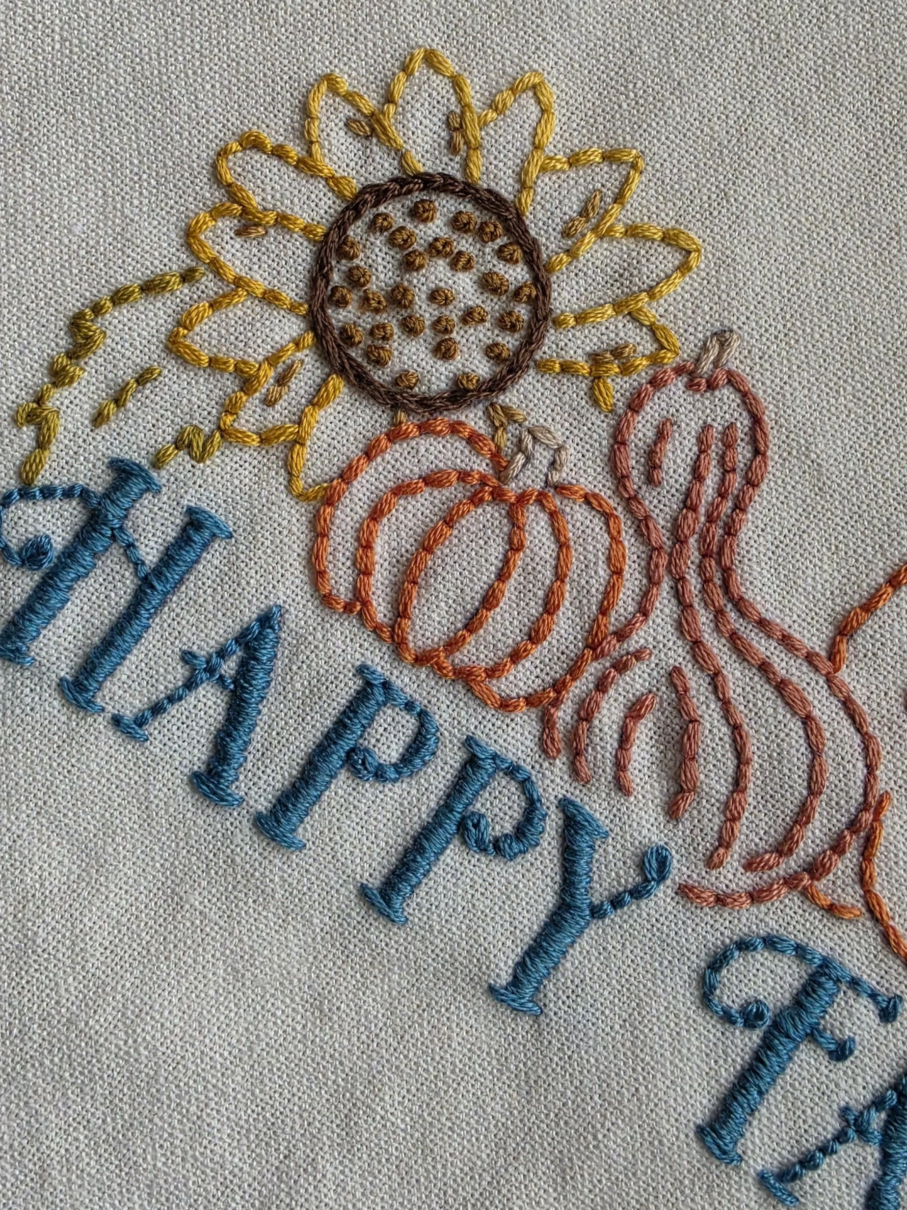 Close-up of hand embroidery showing sunflower, pumpkins and colorful stitching on Happy Fall kitchen towel.