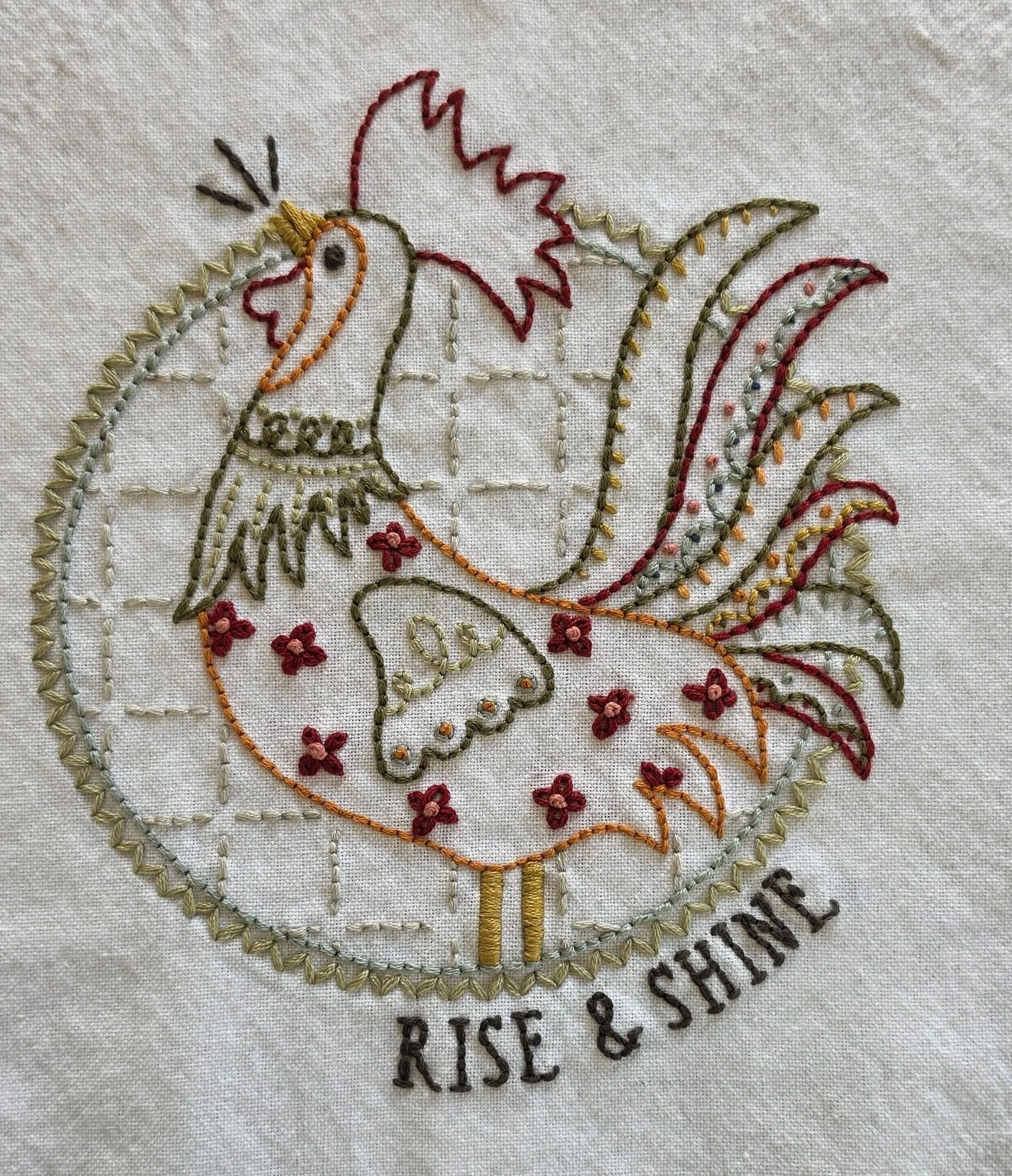 Hand-embroidered Rise & Shine rooster design with colorful folk-art stitching on a cream kitchen towel.