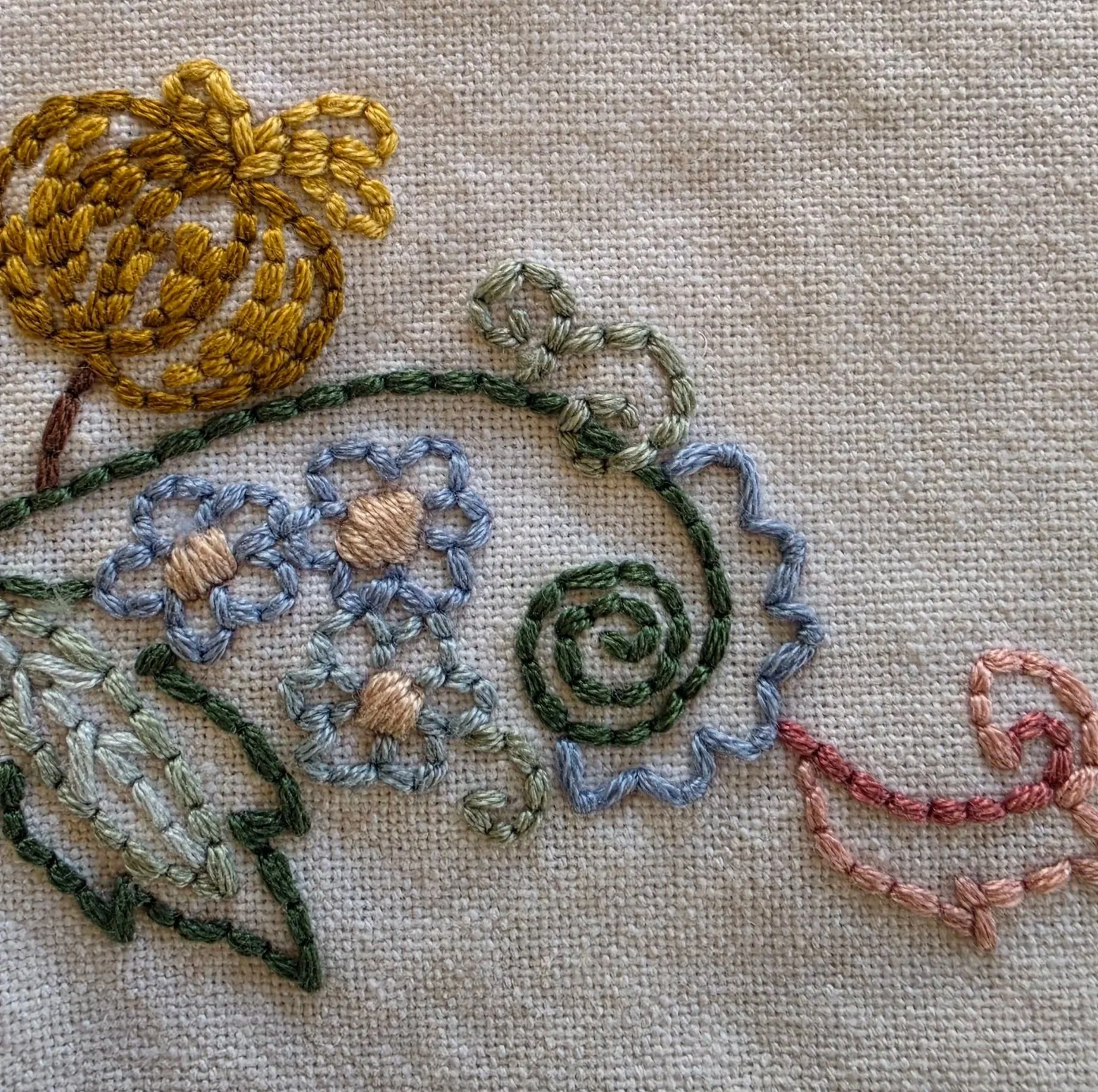 Close-up of blue flowers, golden-yellow embroidered flower, and curling green vine details.