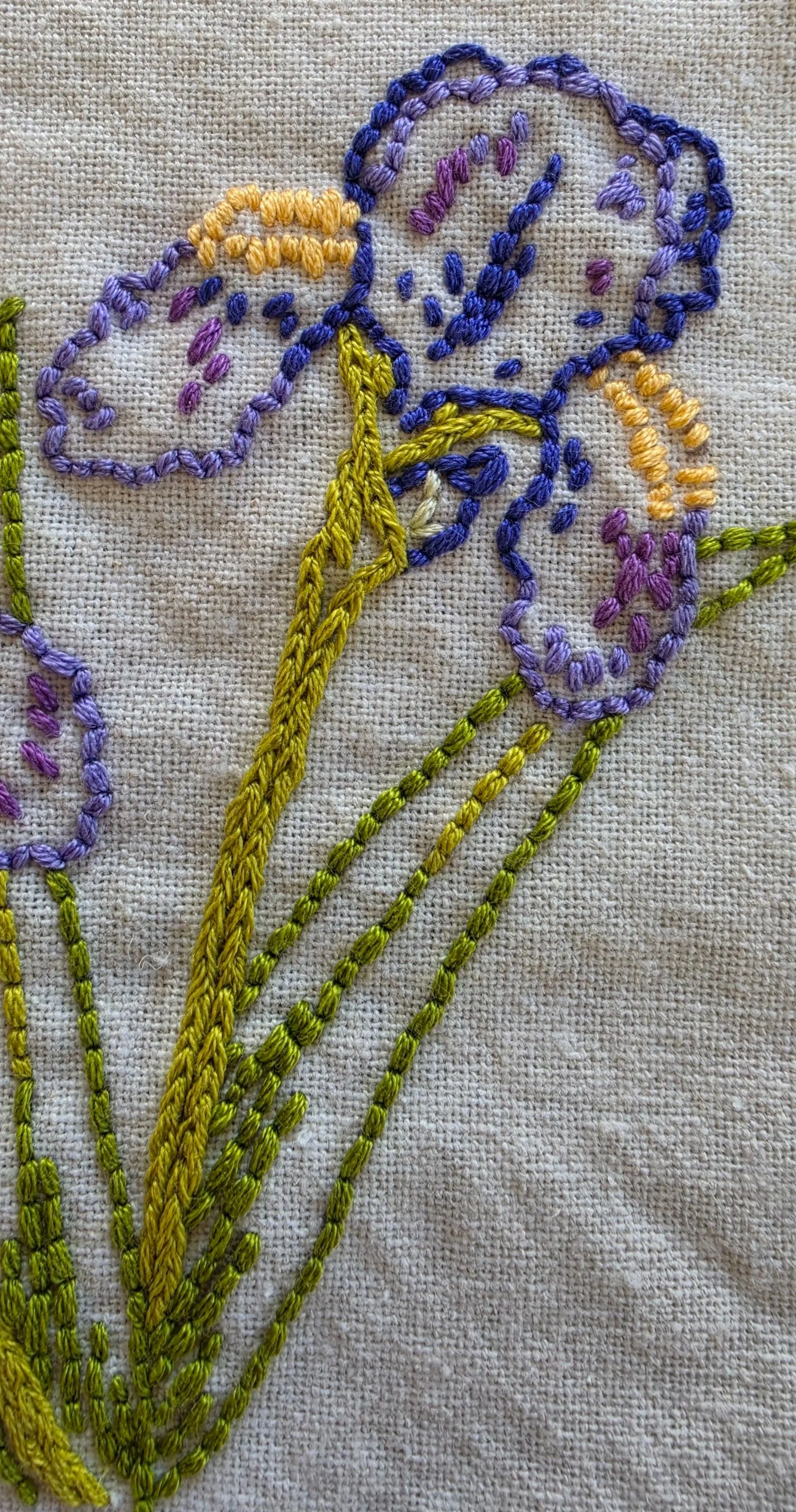 Close-up of colorful iris embroidery and textured green stems on a cream kitchen towel.