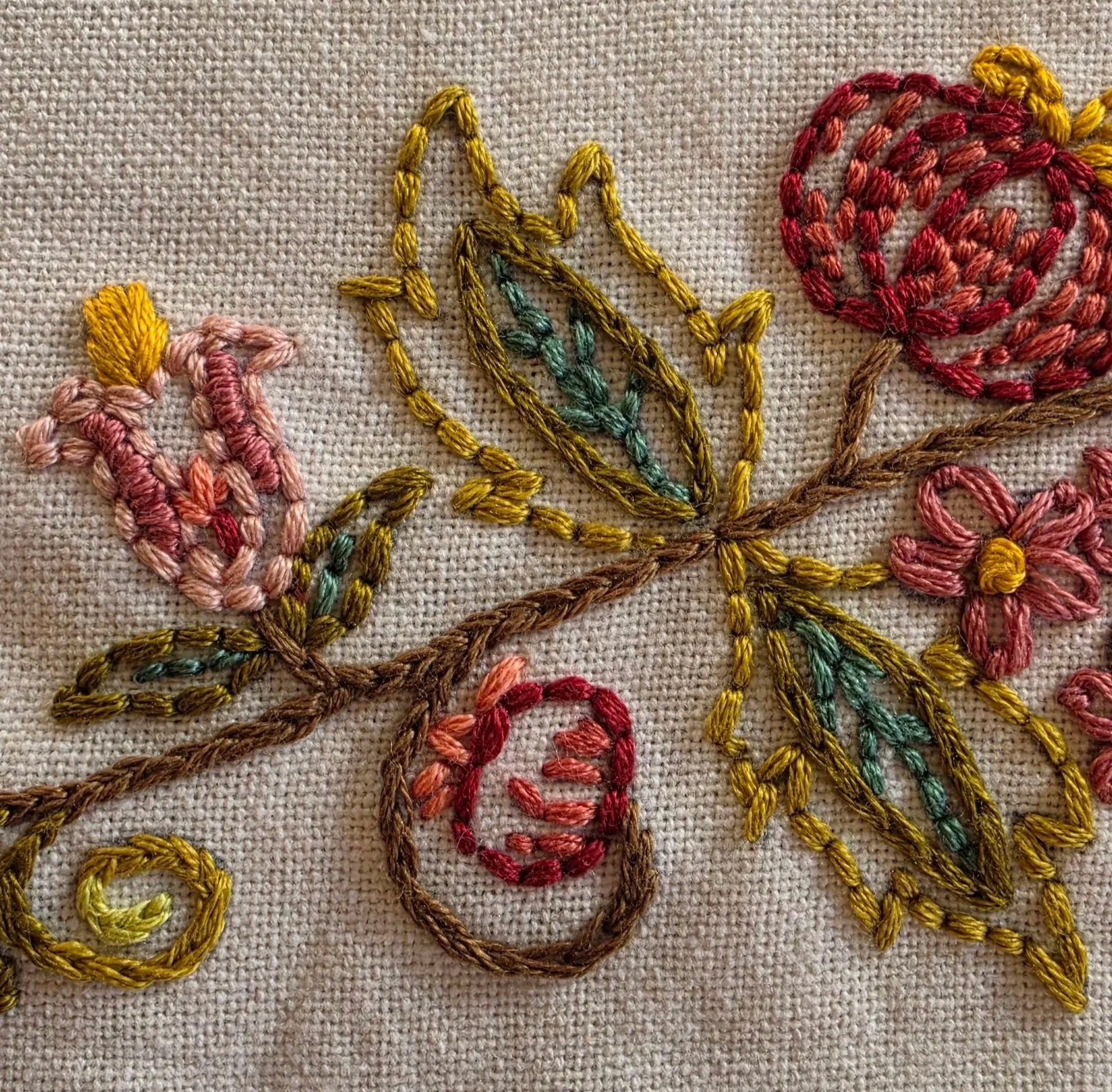 Detailed hand embroidery showing curled green stems, pink and burgundy flowers, and gold accents on a cream kitchen towel.
