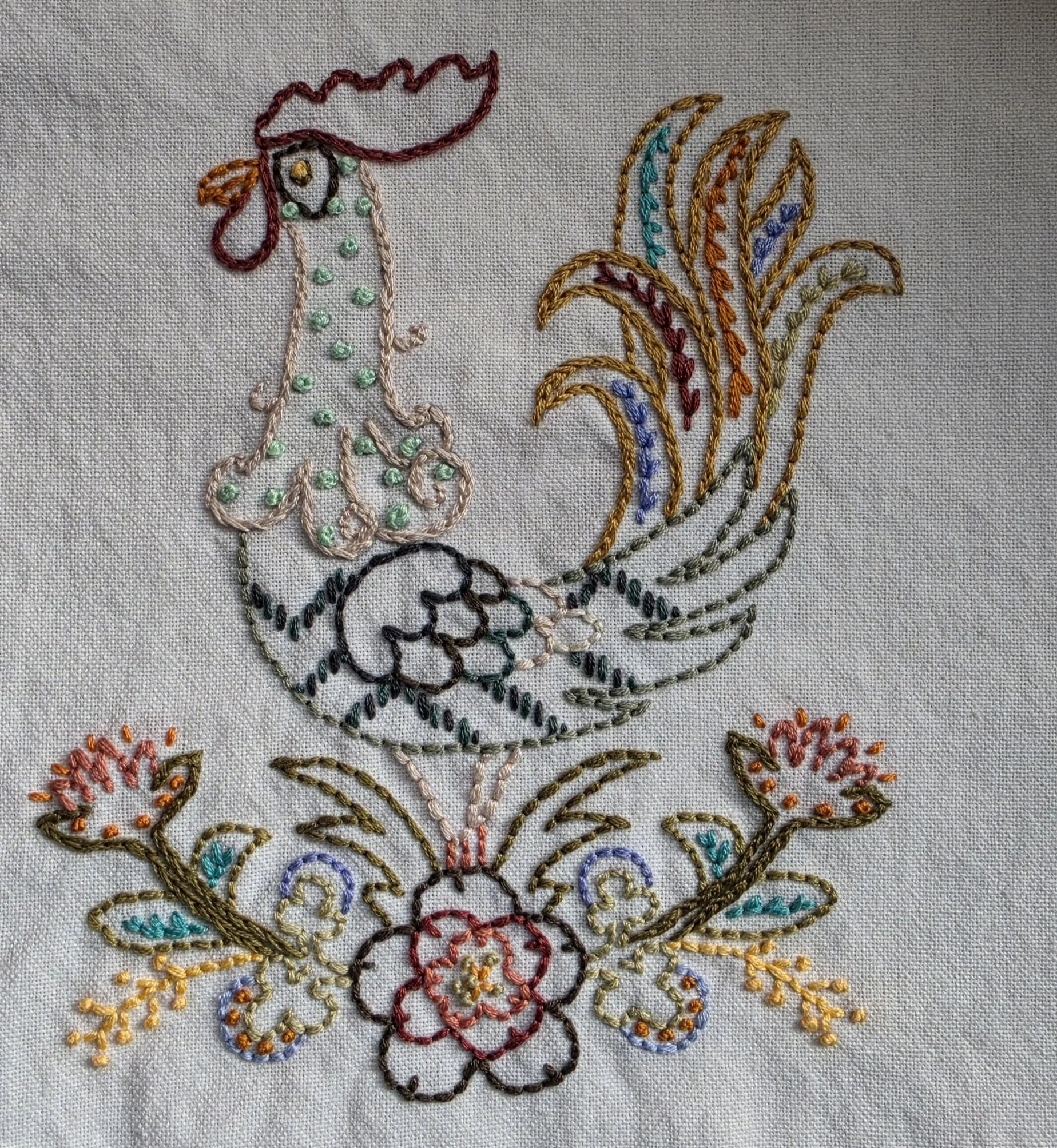 Colorful hand embroidered rooster and floral design on a cream tea towel