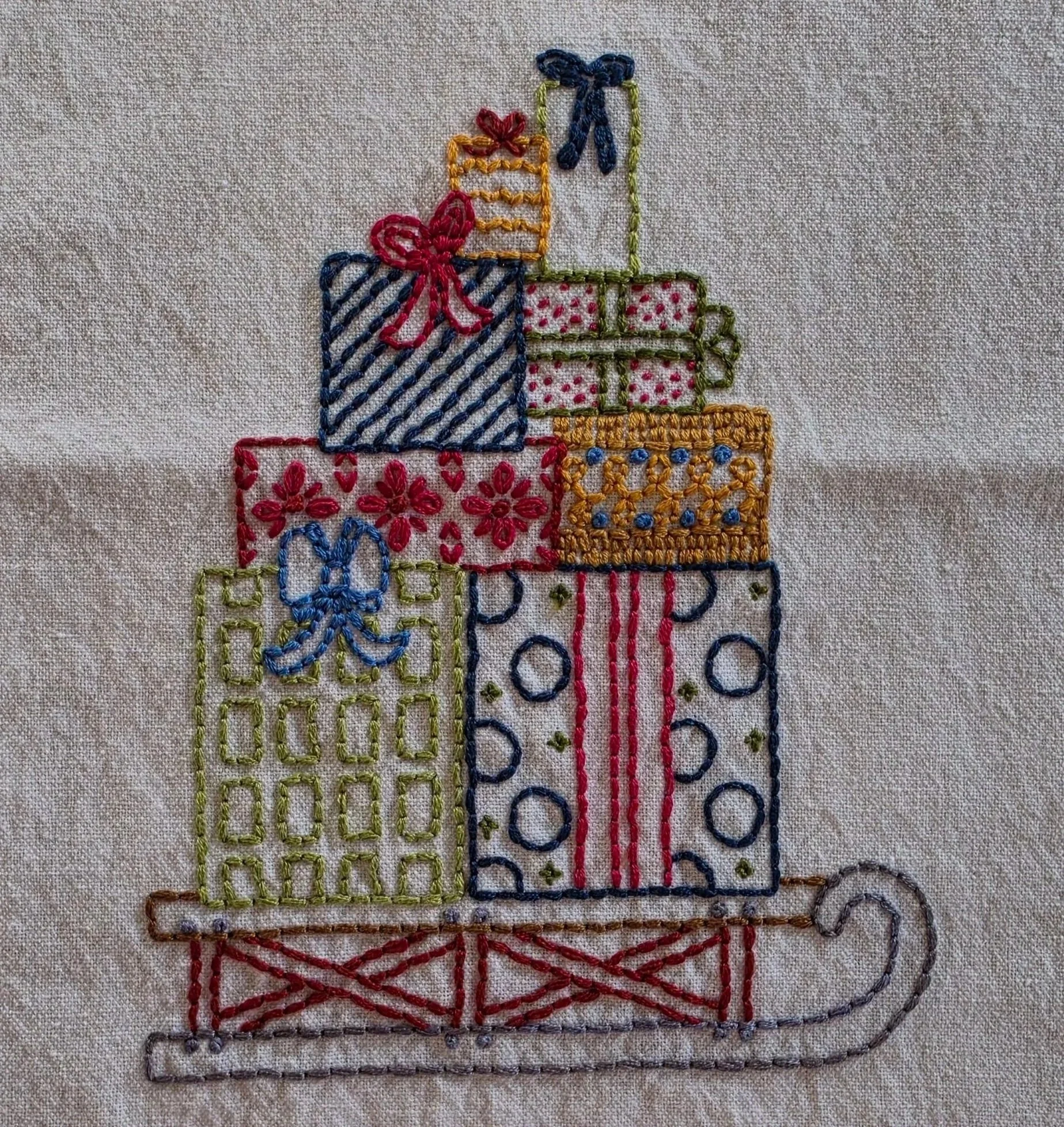 Full view of a hand-embroidered sled topped with colorful Christmas presents and decorative bows.