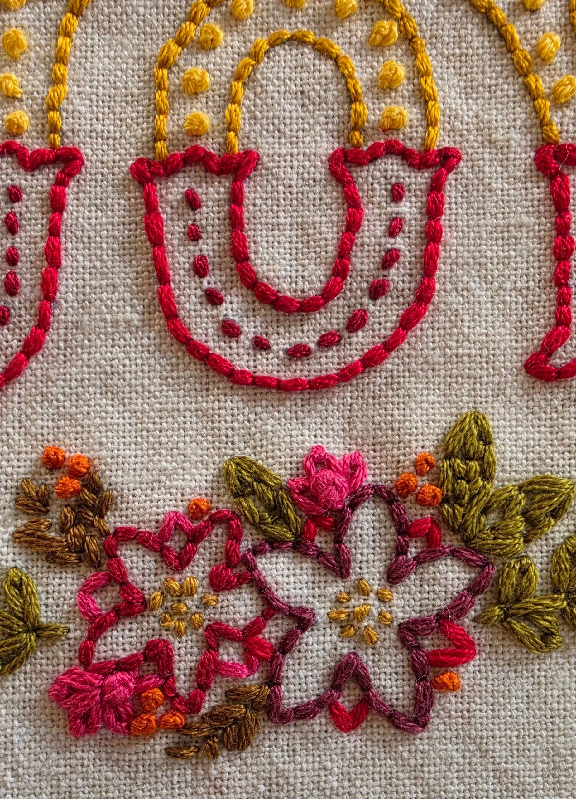 Close-up of pink and red embroidered flowers and green leaves on the JOY towel.