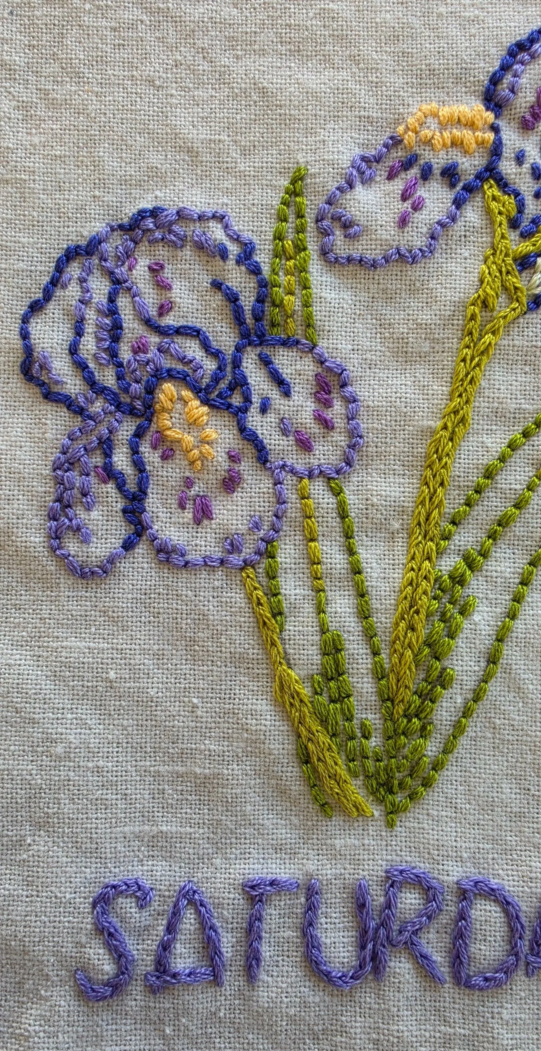 Detail of hand-embroidered purple iris petals with golden-yellow accents.