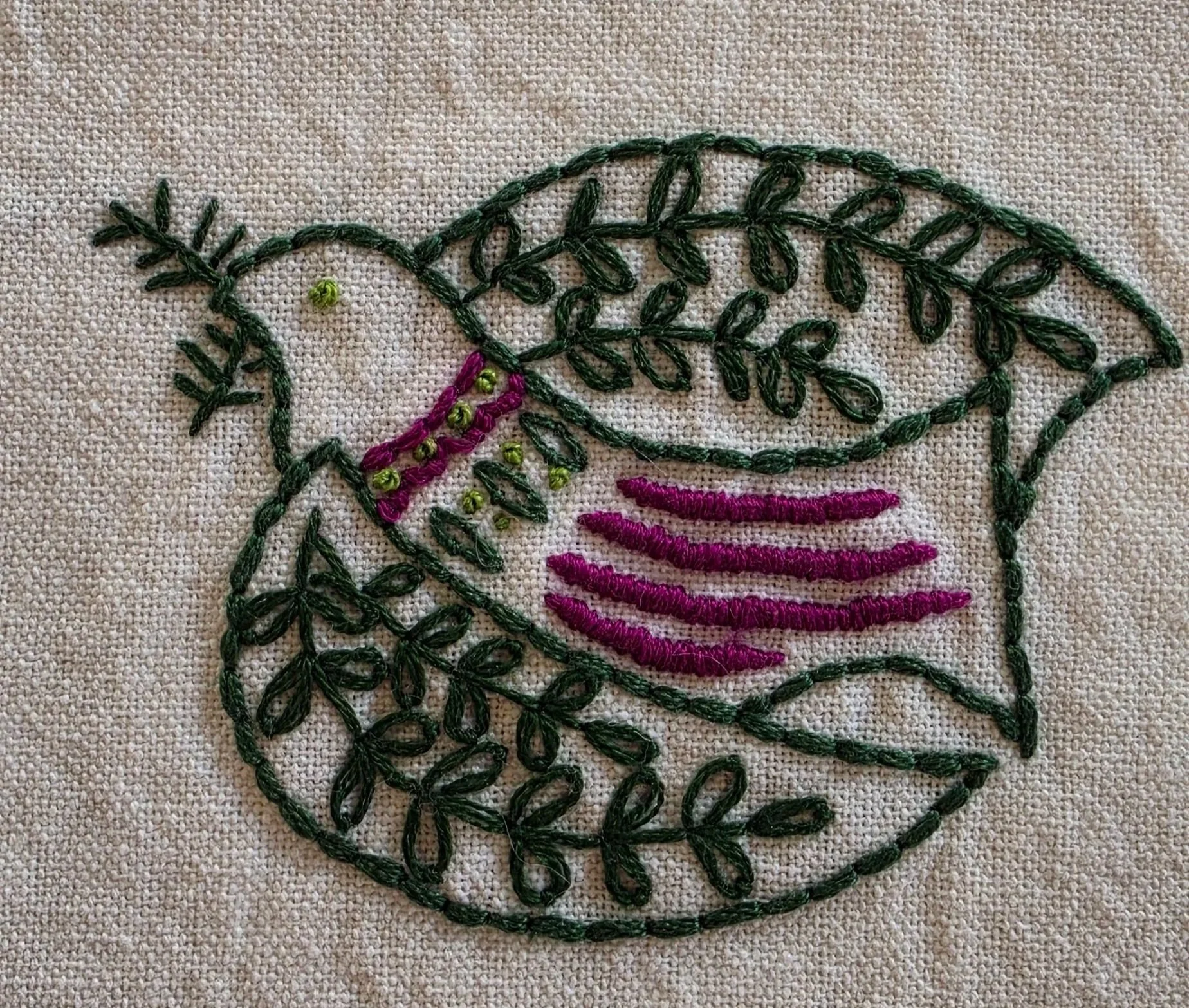 Full view of a whimsical bird embroidered in green and plum thread on natural-colored fabric.