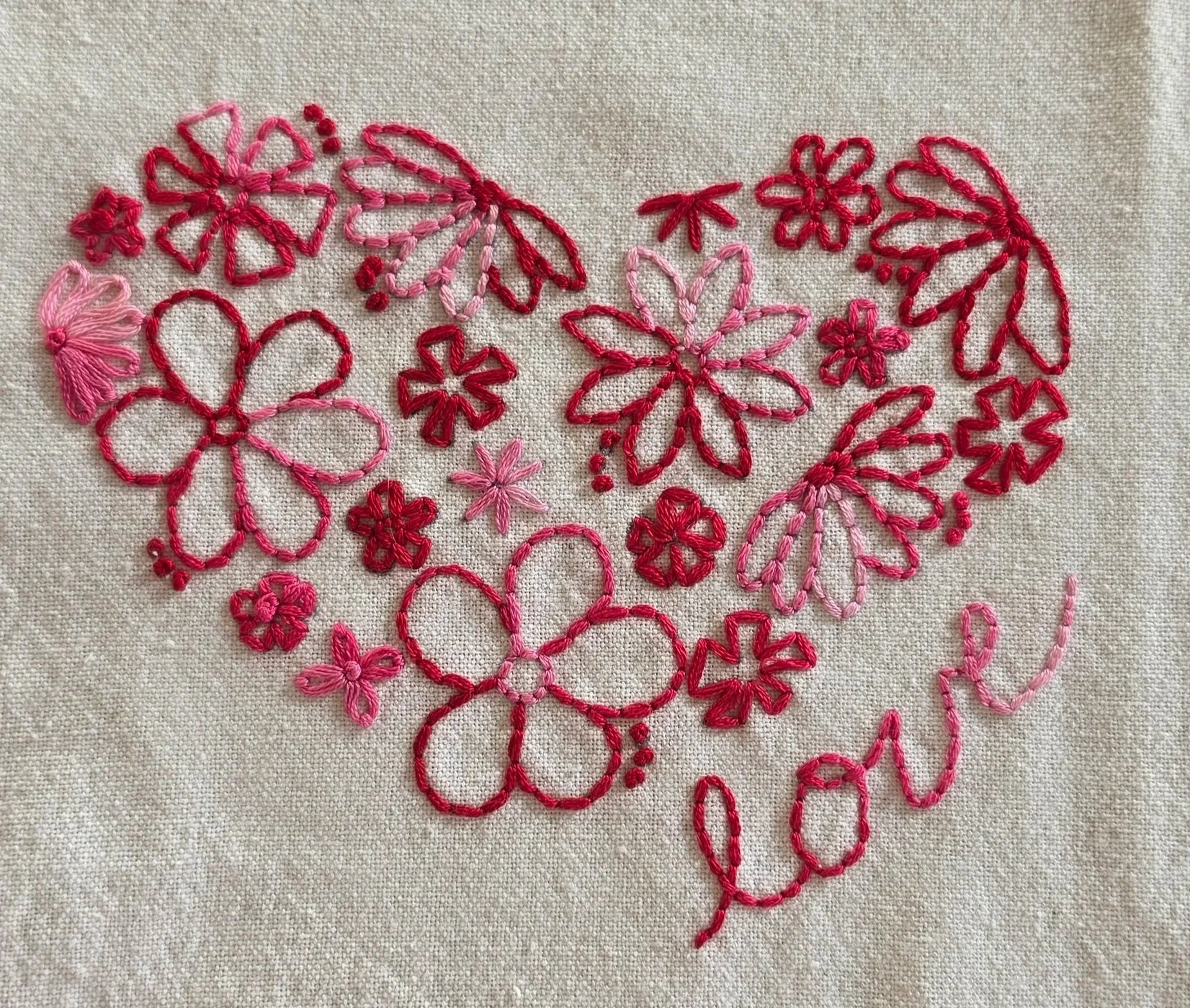 Full view of a heart-shaped floral embroidery design in red and pink thread with the word love on a white cotton towel.