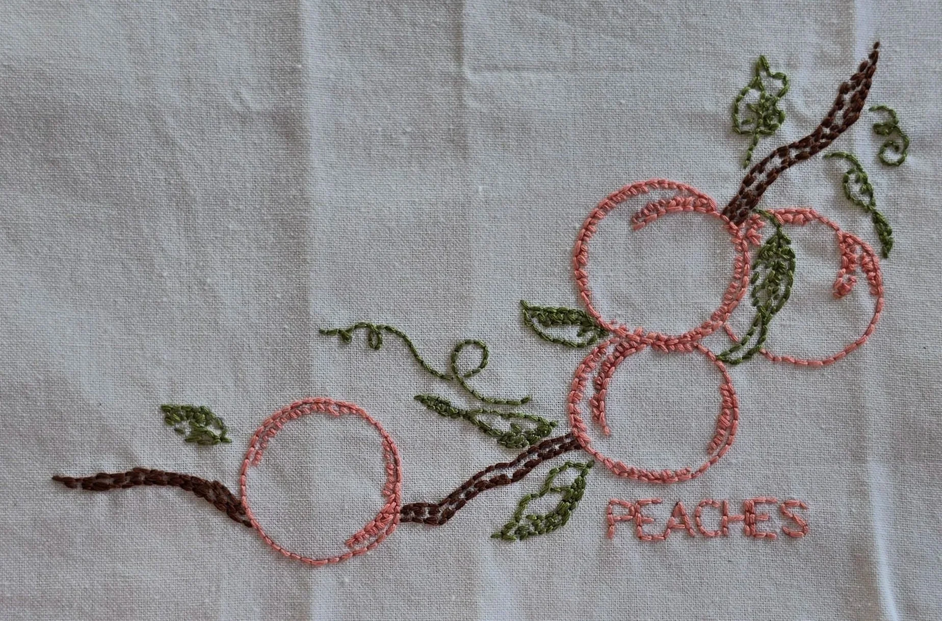 Full view of peach branch embroidery with coral peach outlines, green leaves, brown stems, and PEACHES lettering.