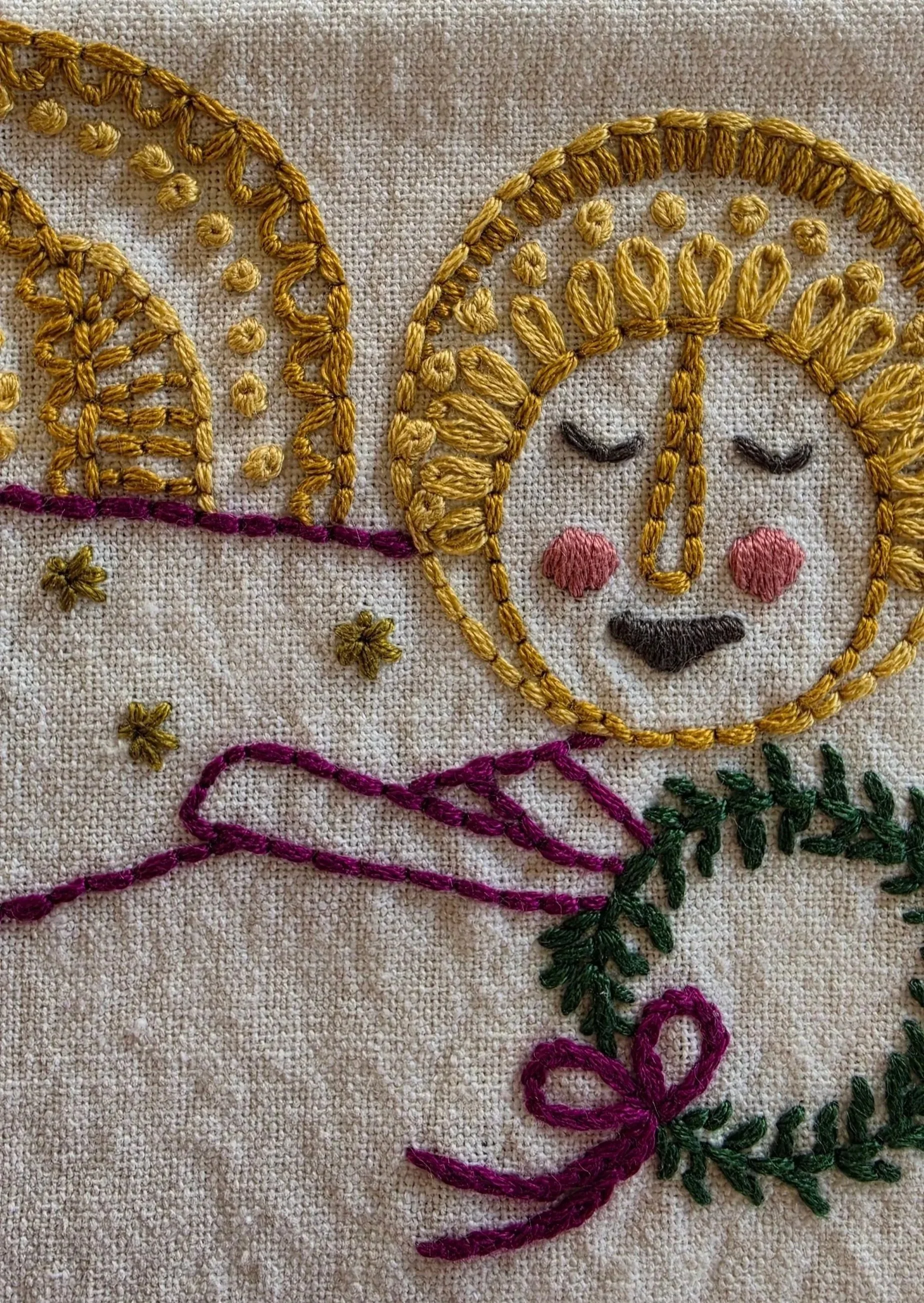 Detailed view of the angel's embroidered face and golden halo on a natural-colored kitchen towel.