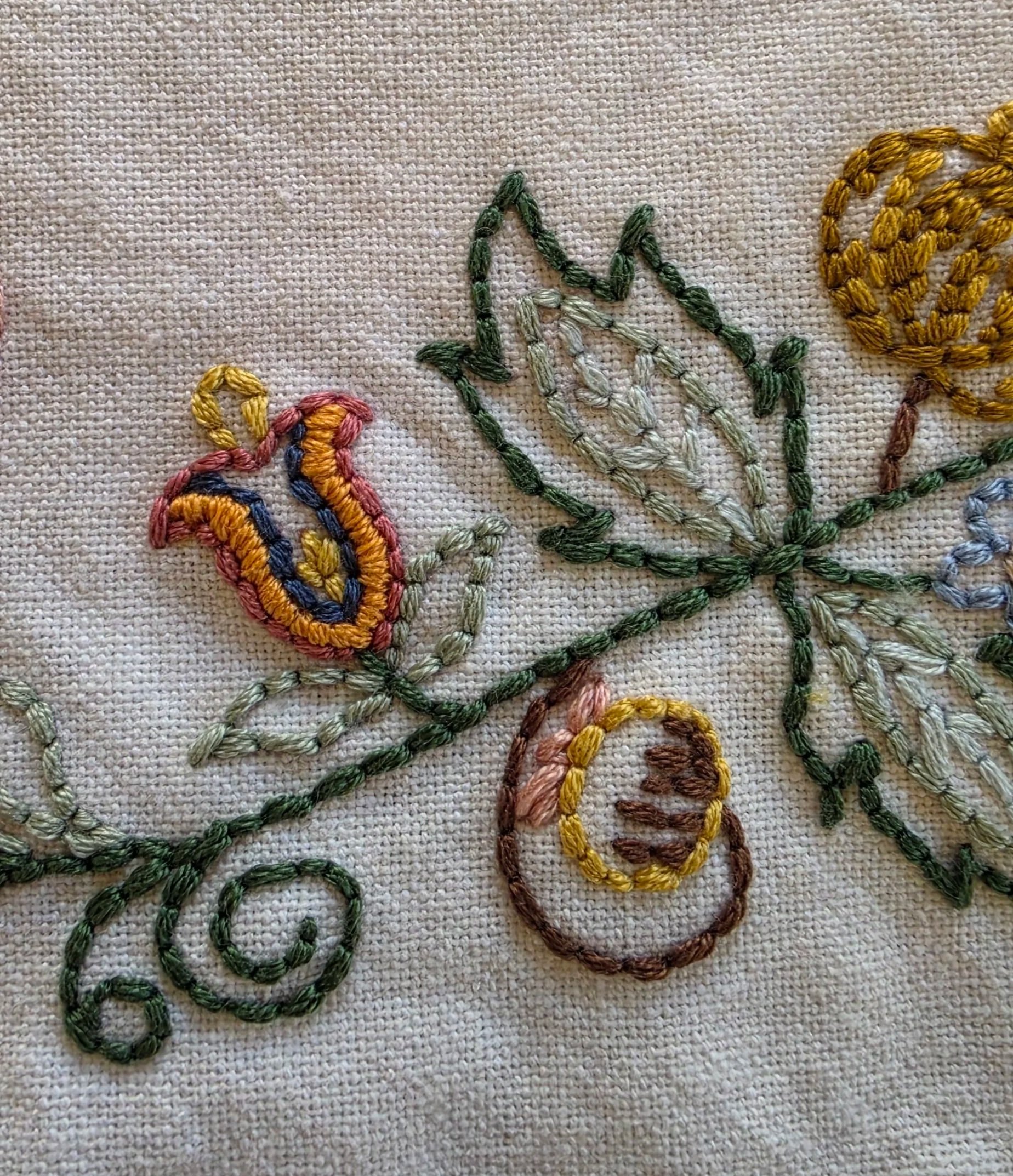 Detailed hand embroidery featuring colorful floral motifs, green leaves, and decorative stitching.